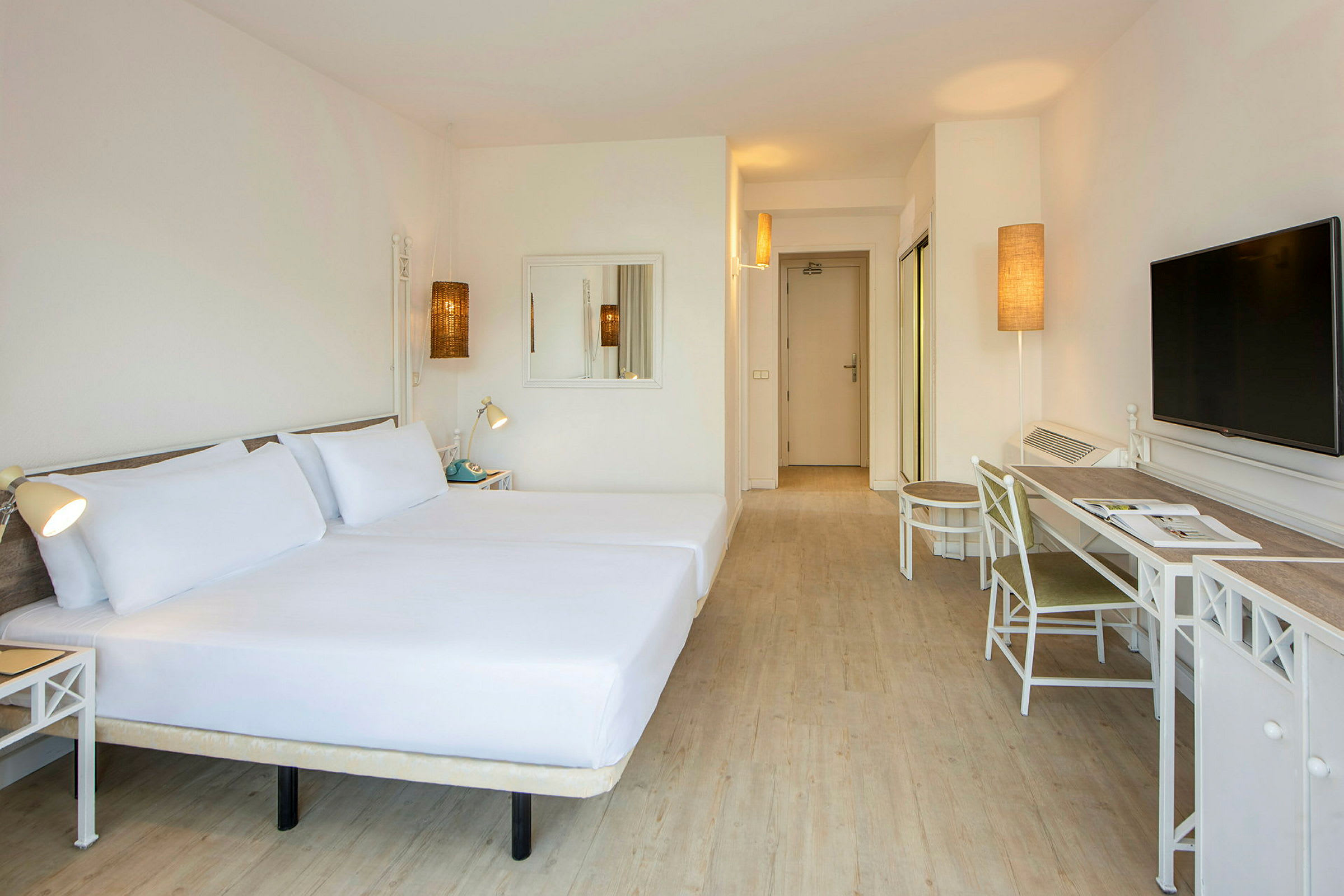 Hotellihuone, jossa on kaksi sänkyä vasemmalla, kirjoituspöytä tuolilla oikealla ja televisio seinällä. (Tekoälyn luoma teksti)