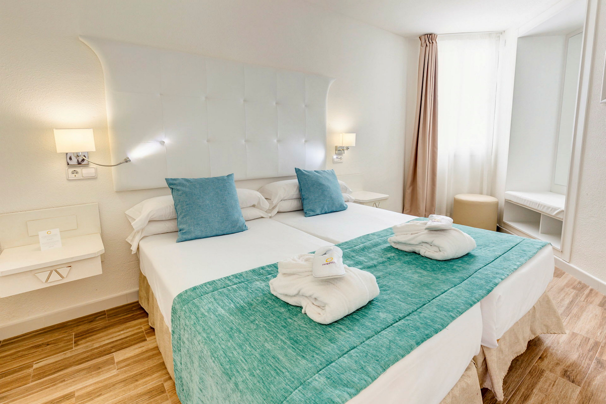 Hotellihuone, jossa on parivuode, valkoiset lakanat ja vaaleansiniset tyynyt. (Tekoälyn luoma teksti)