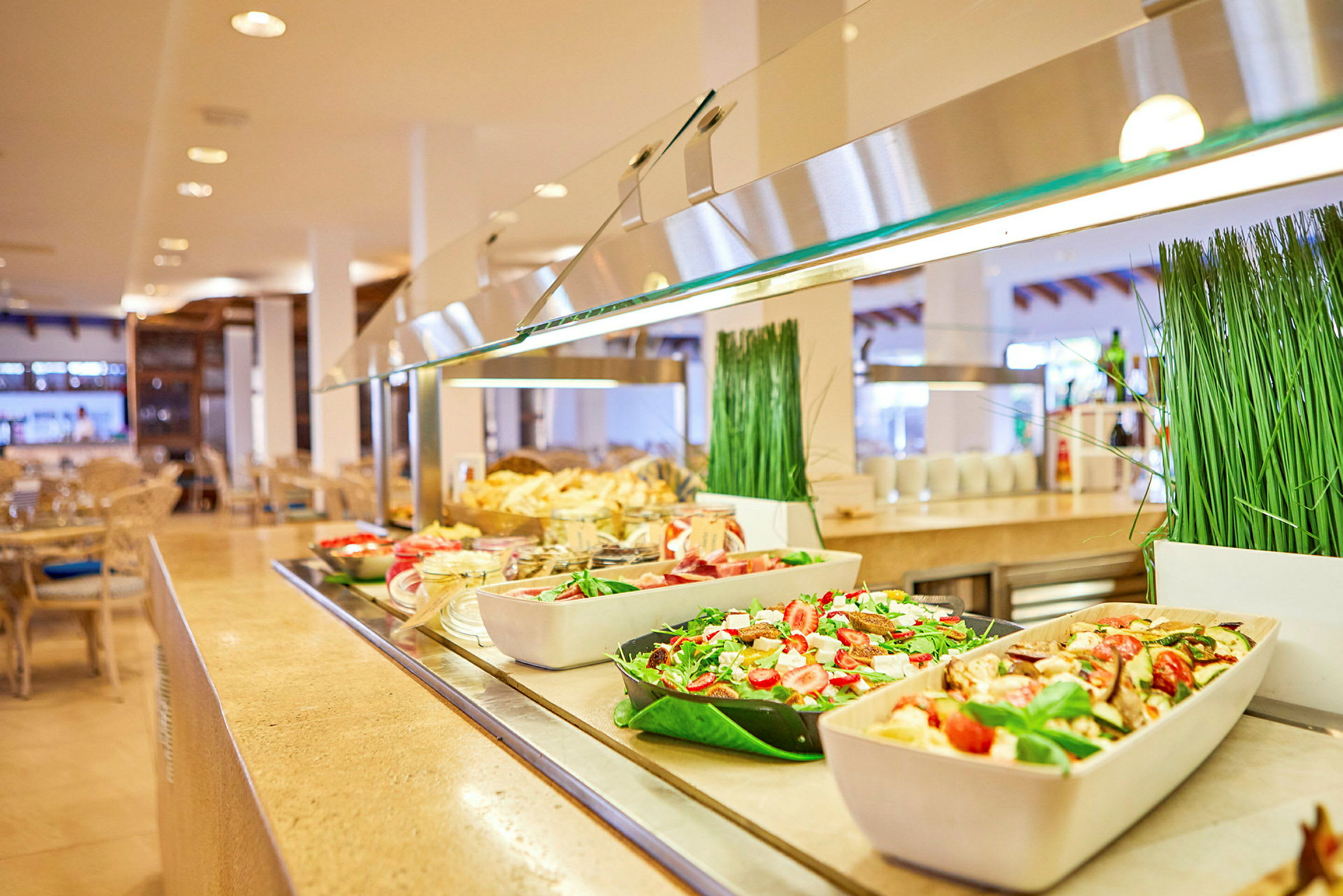 Buffet-pöytä, jossa erilaisia ruokia, kuten salaatteja ja hedelmiä, valoisassa ruokasalissa. (Tekoälyn luoma teksti)