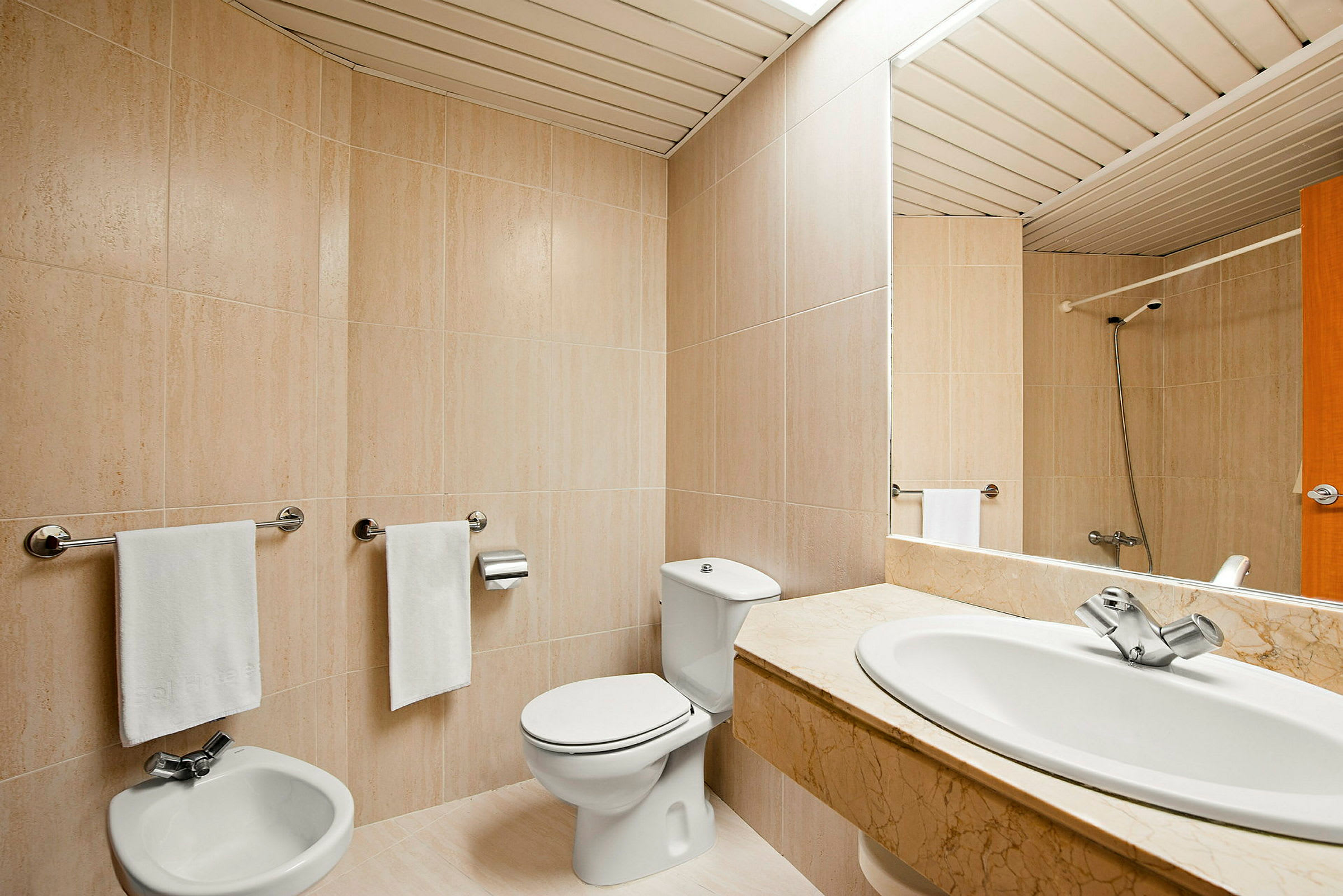 Kylpyhuone, jossa on beige laattoitus, wc, bidee ja marmorialtas. (Tekoälyn luoma teksti)