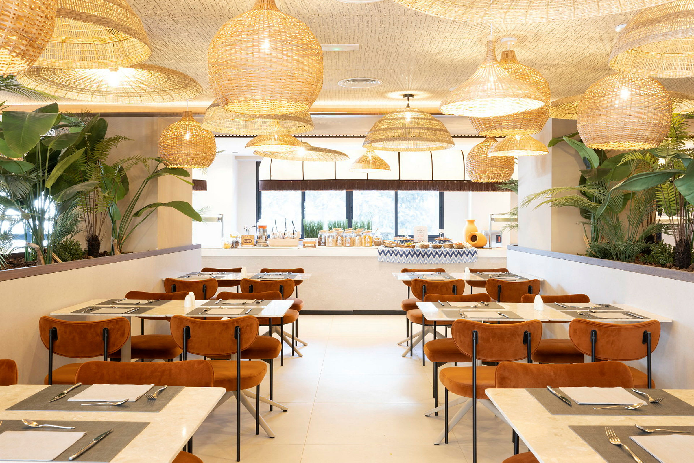 Tyylikäs ravintola, jossa on modernit huonekalut, suuret ikkunat, kasveja ja kattokorit. (Tekoälyn luoma teksti)
