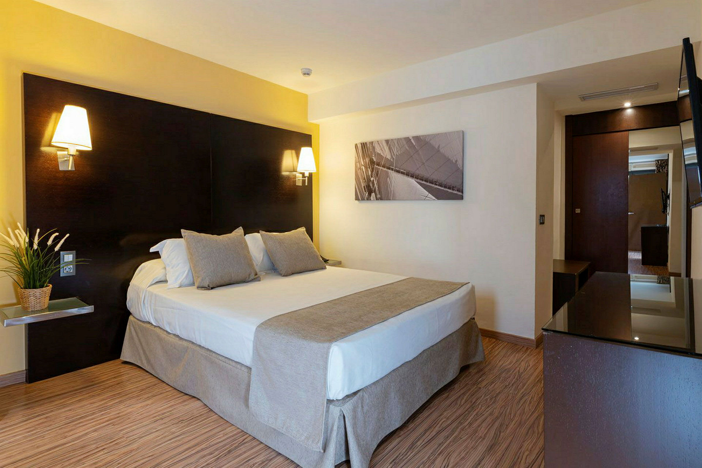 Hotellihuone, jossa on parivuode, yöpöytävalaisimet ja taulu seinällä. (Tekoälyn luoma teksti)