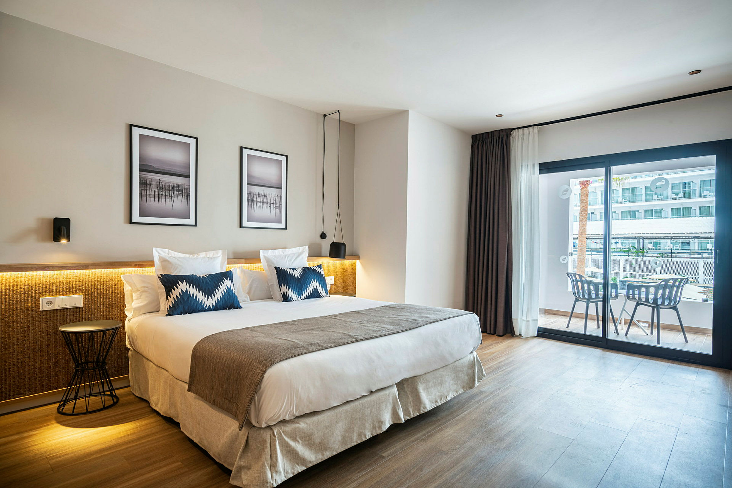 Hotellihuone, jossa on suuri sänky, kaksi tyynyä ja moderni sisustus sekä parveke istuimineen. (Tekoälyn luoma teksti)