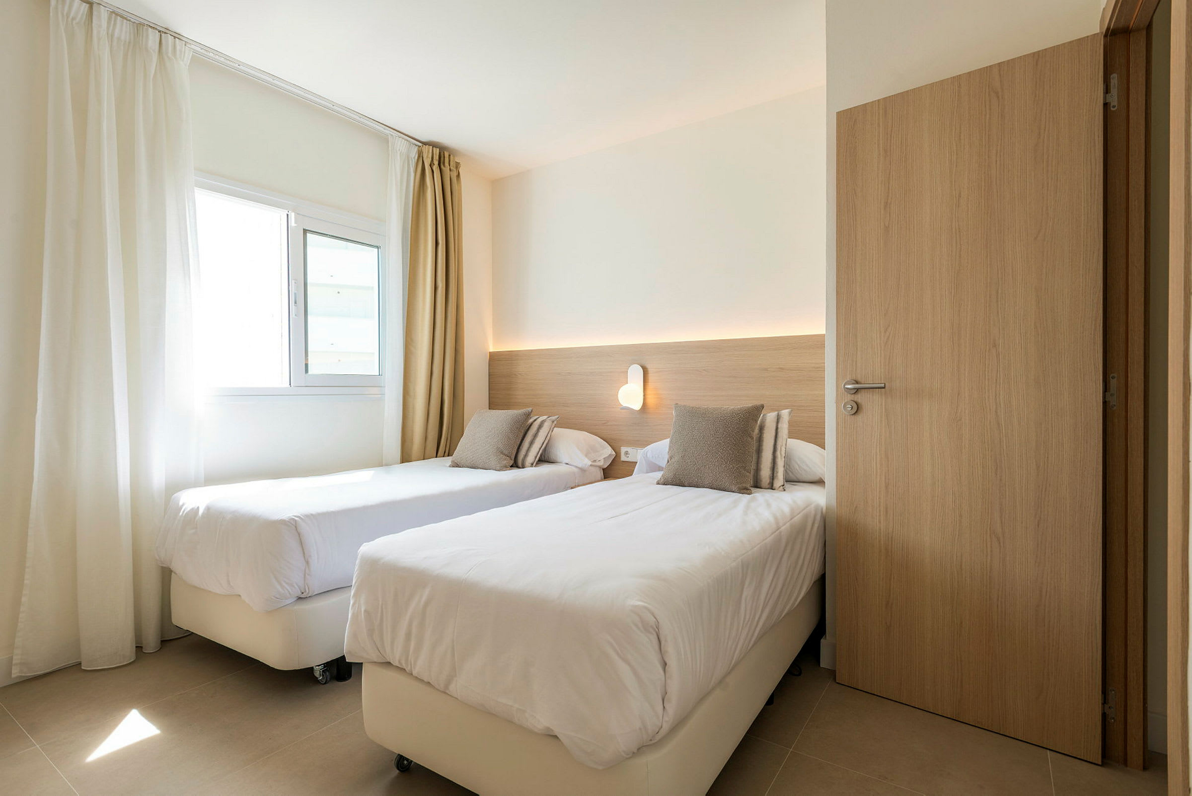 Hotellihuone, jossa kaksi erillistä sänkyä ja seinälamppu. (Tekoälyn luoma teksti)