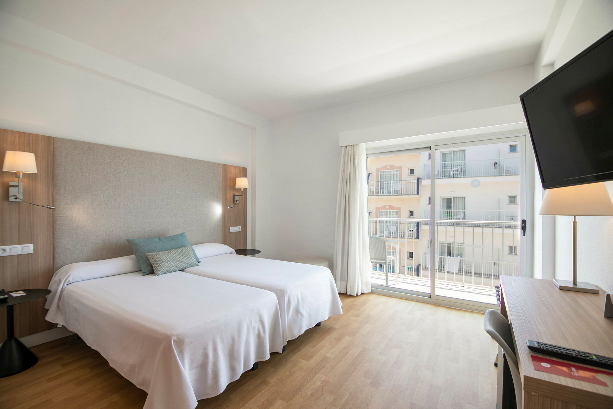 Hotellihuone, jossa on kaksi erillistä vuodetta ja parvekkeen ovi. (Tekoälyn luoma teksti)