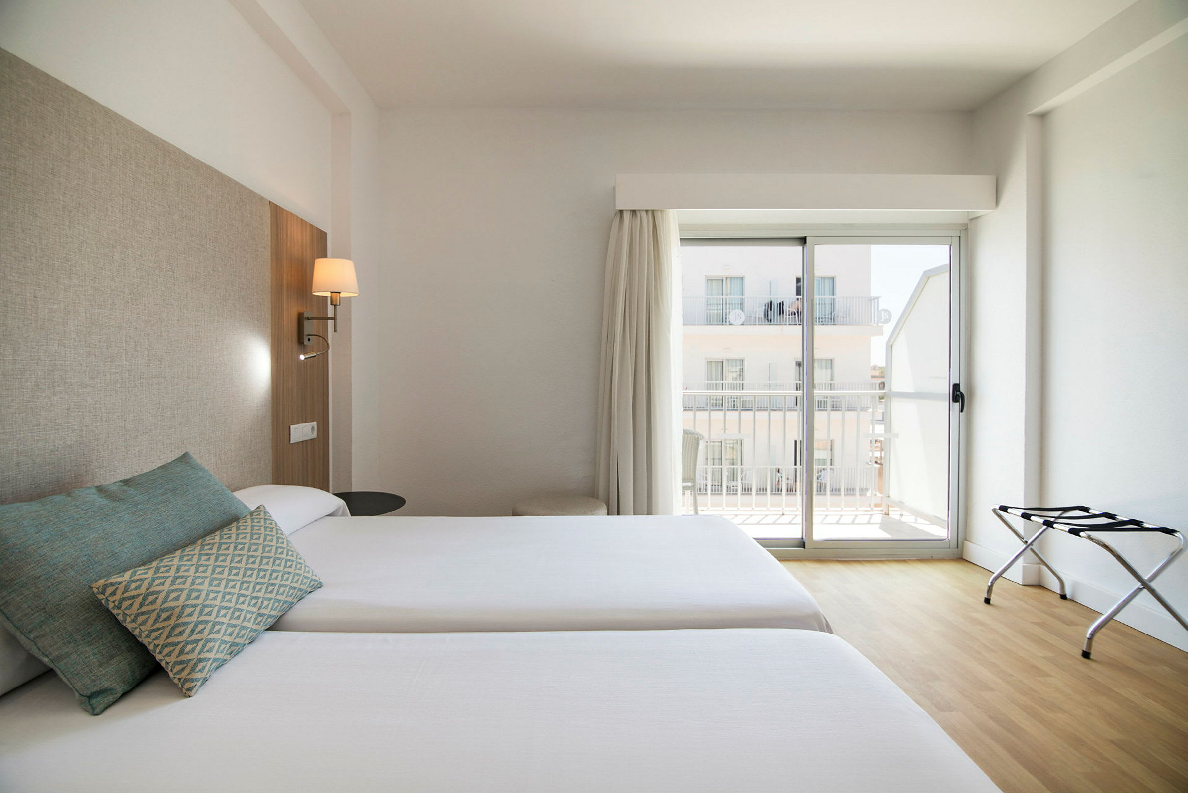 Kaksi erillistä vuodetta hotellihuoneessa, jossa on vaalea sisustus ja ikkuna parvekkeelle. (Tekoälyn luoma teksti)