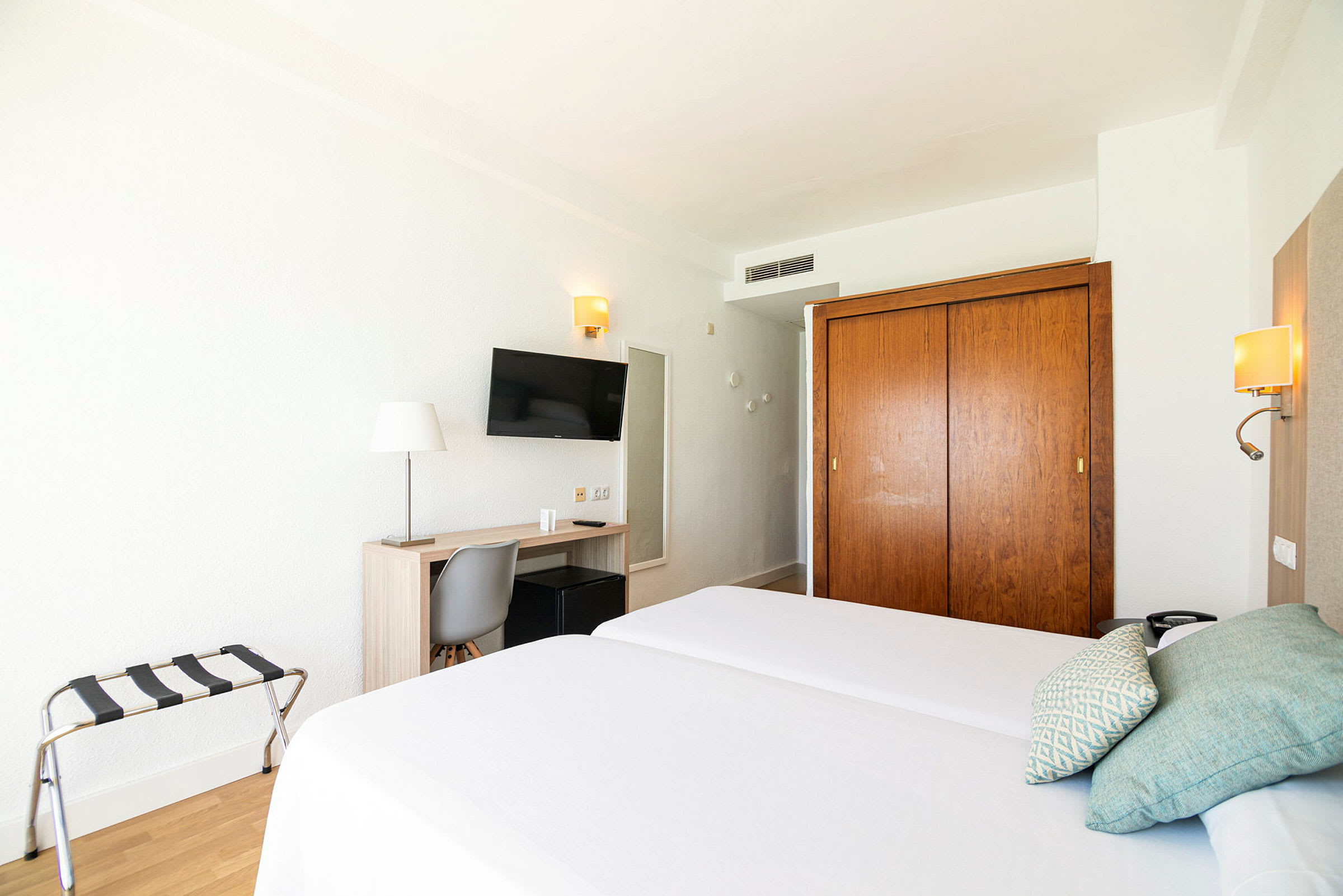 Hotellihuone, jossa kaksi erillistä vuodetta, kirjoituspöytä, tuoli, televisio ja vaatekaappi. (Tekoälyn luoma teksti)