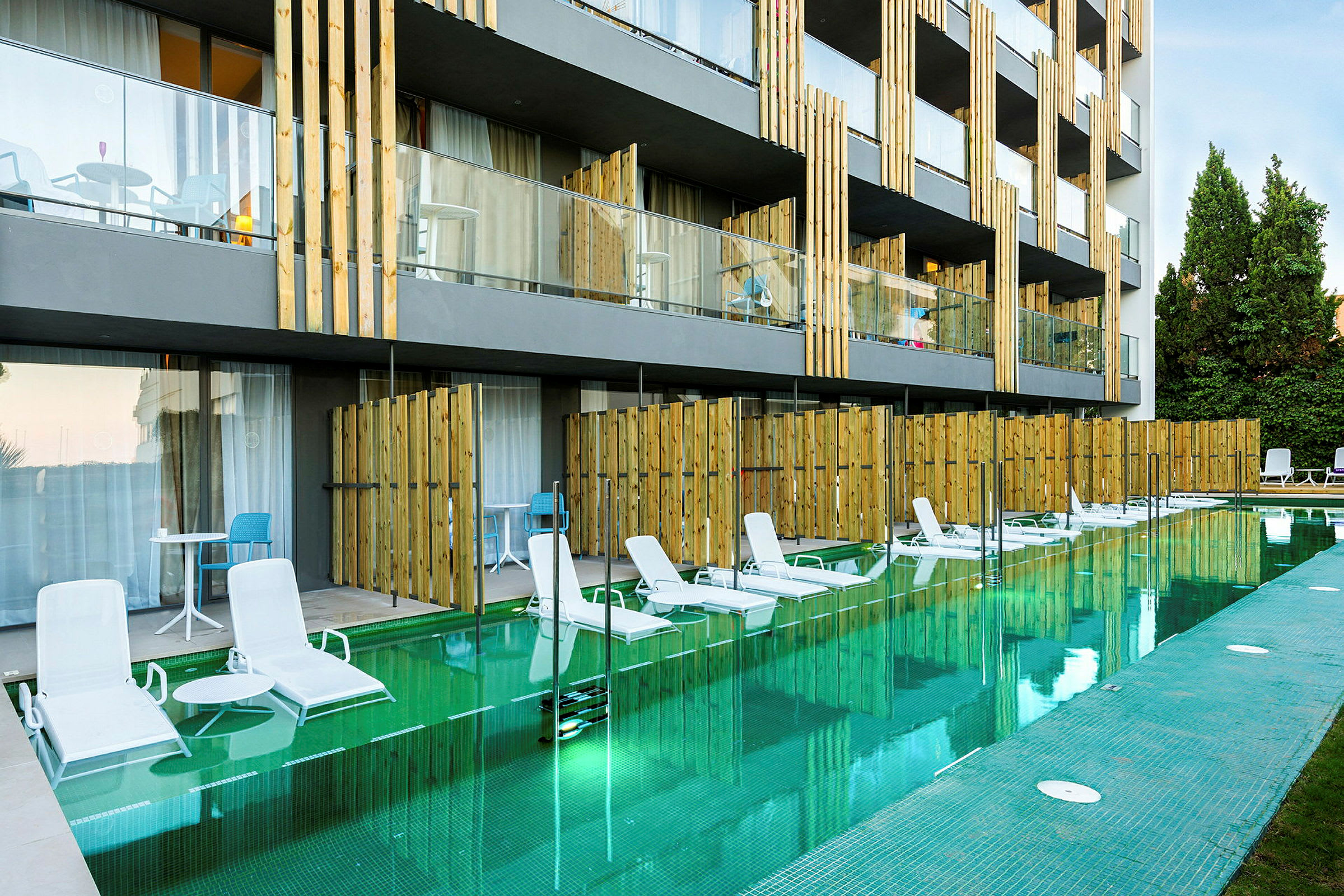 Kuva hotellista, jossa on suora pääsy altaaseen joistakin huoneista. Aurinkotuoleja altaan reunan varrella. (Tekoälyn luoma teksti)