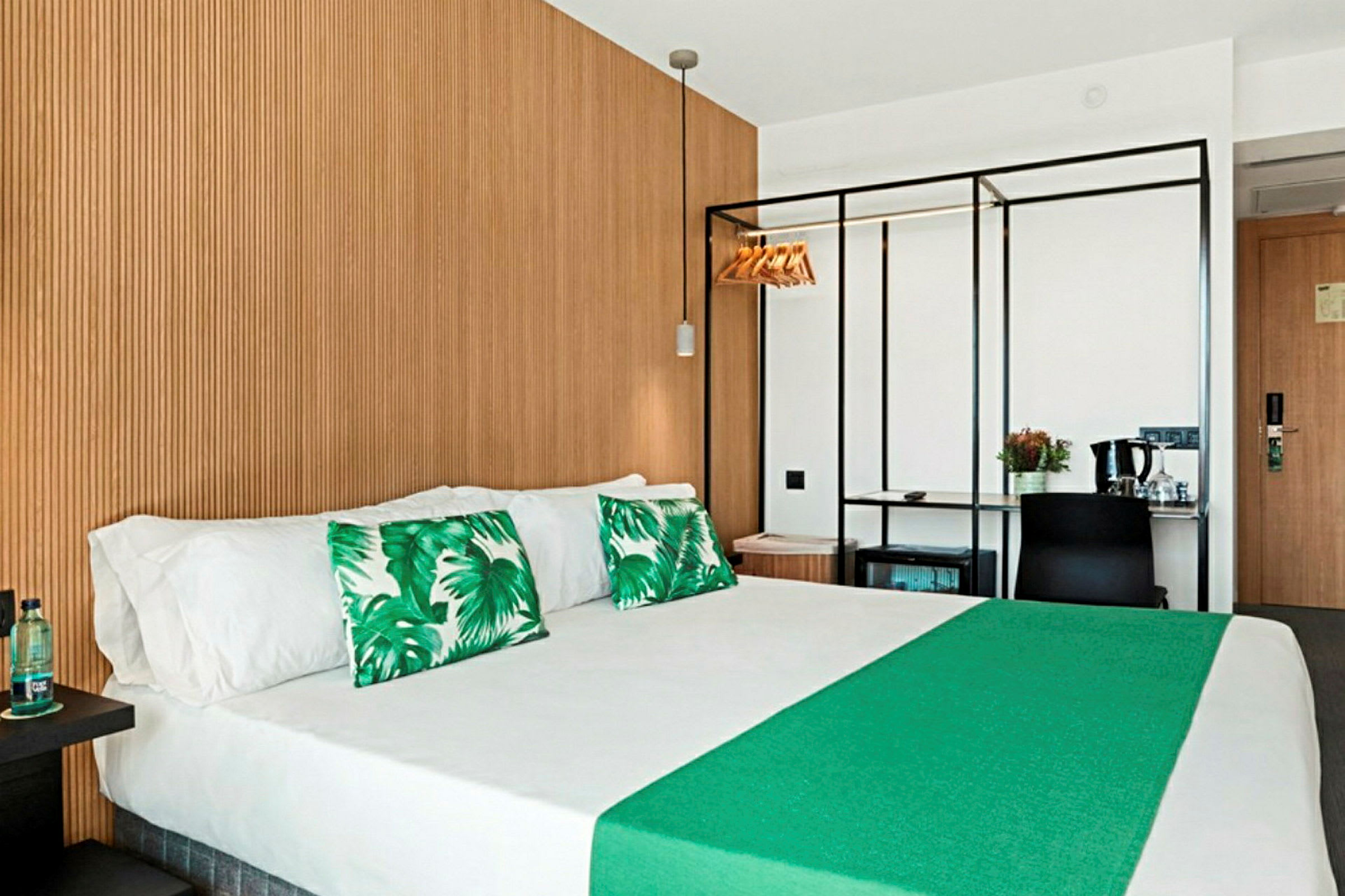 Hotellihuone, jossa parivuode, vihreät koristetyynyt ja puupaneelikuvio seinässä. (Tekoälyn luoma teksti)