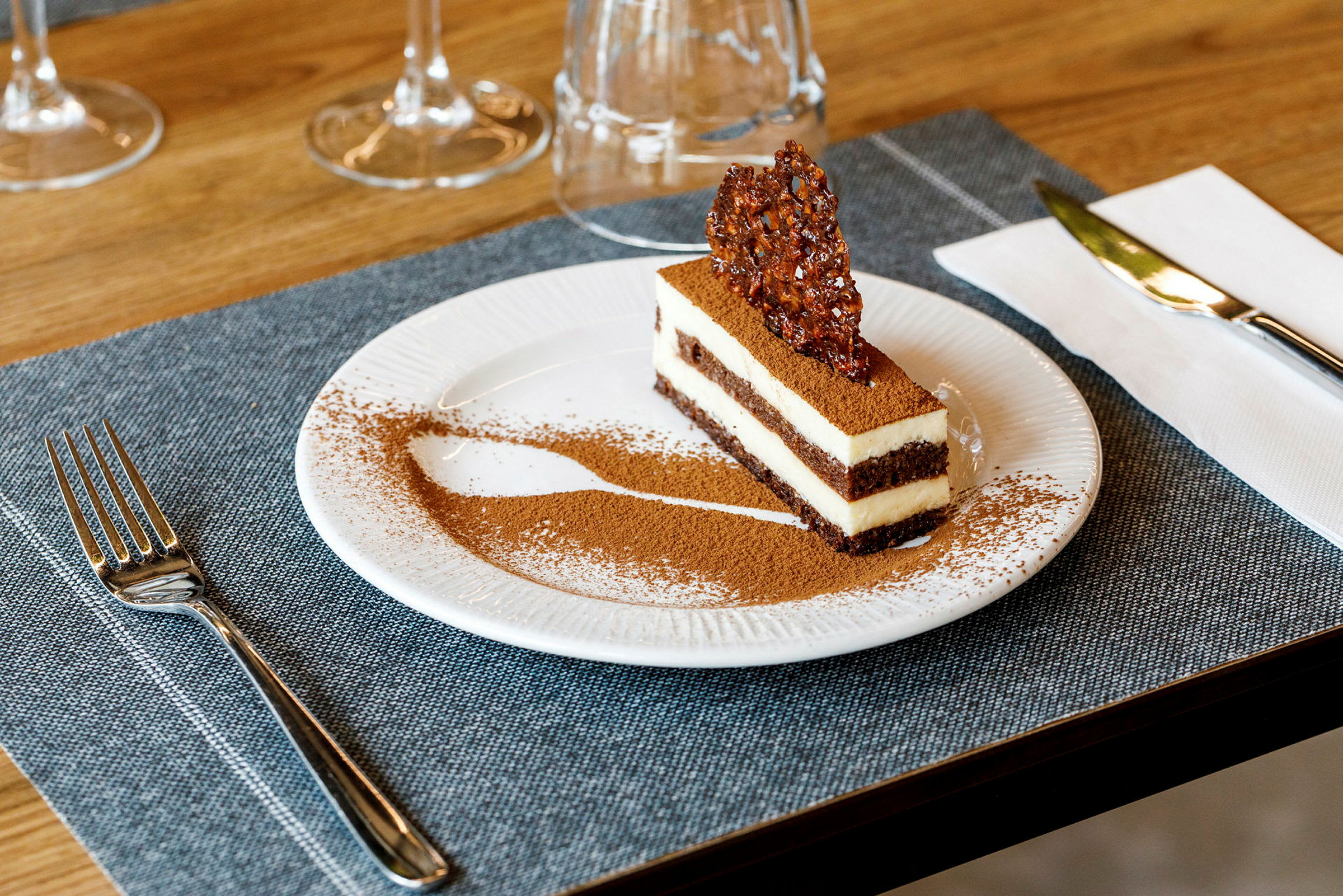 Jälkiruoka, luultavasti tiramisu, tarjoiltu lautasella, koristeltuna kaakaojauheella ja rapealla karamellipalalla päällä. (Tekoälyn luoma teksti)