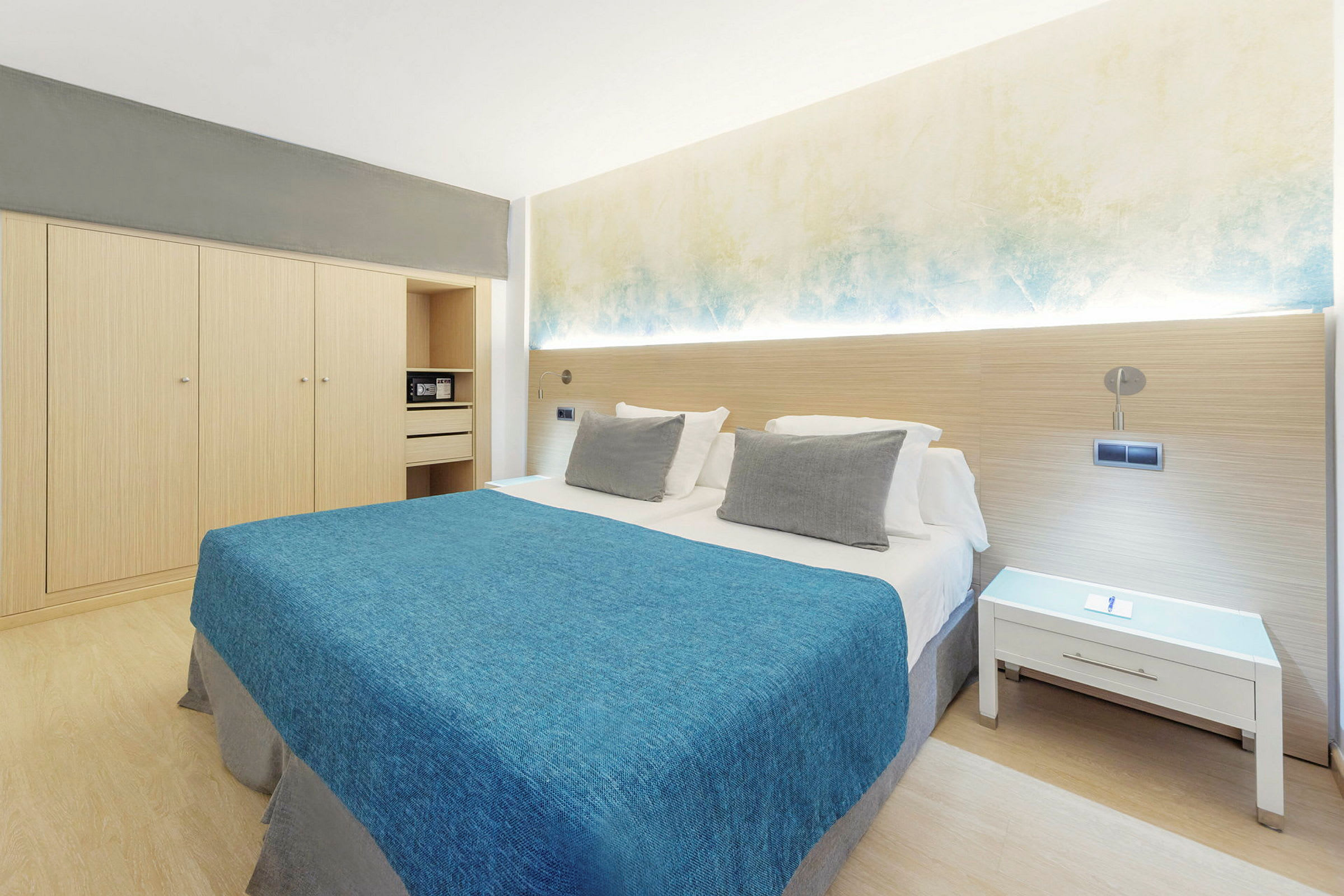 Hotellihuone, jossa parivuode, sininen päiväpeite, valkoiset tyynyt ja minimalistinen sisustus. (Tekoälyn luoma teksti)