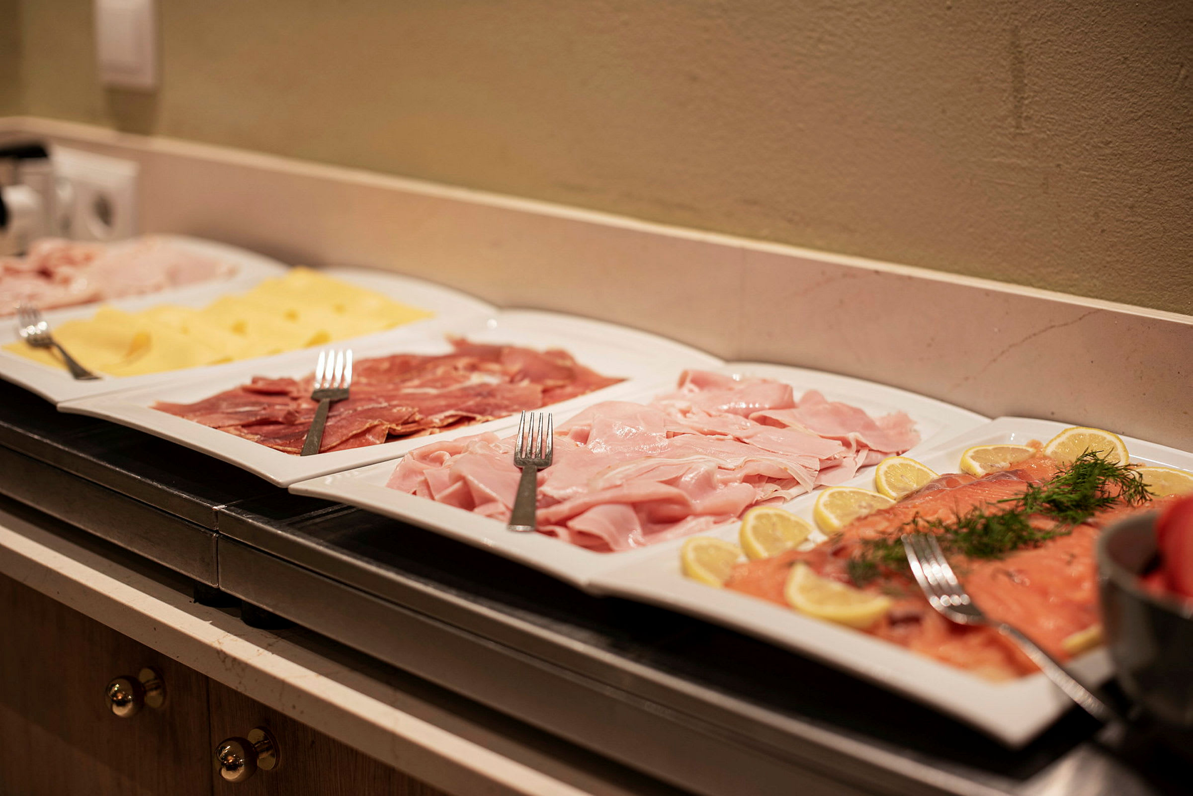 Tarjottimet, joissa on erilaisia kylmiä leikkeleitä ja juustoa, aseteltuina buffetissa. (Tekoälyn luoma teksti)