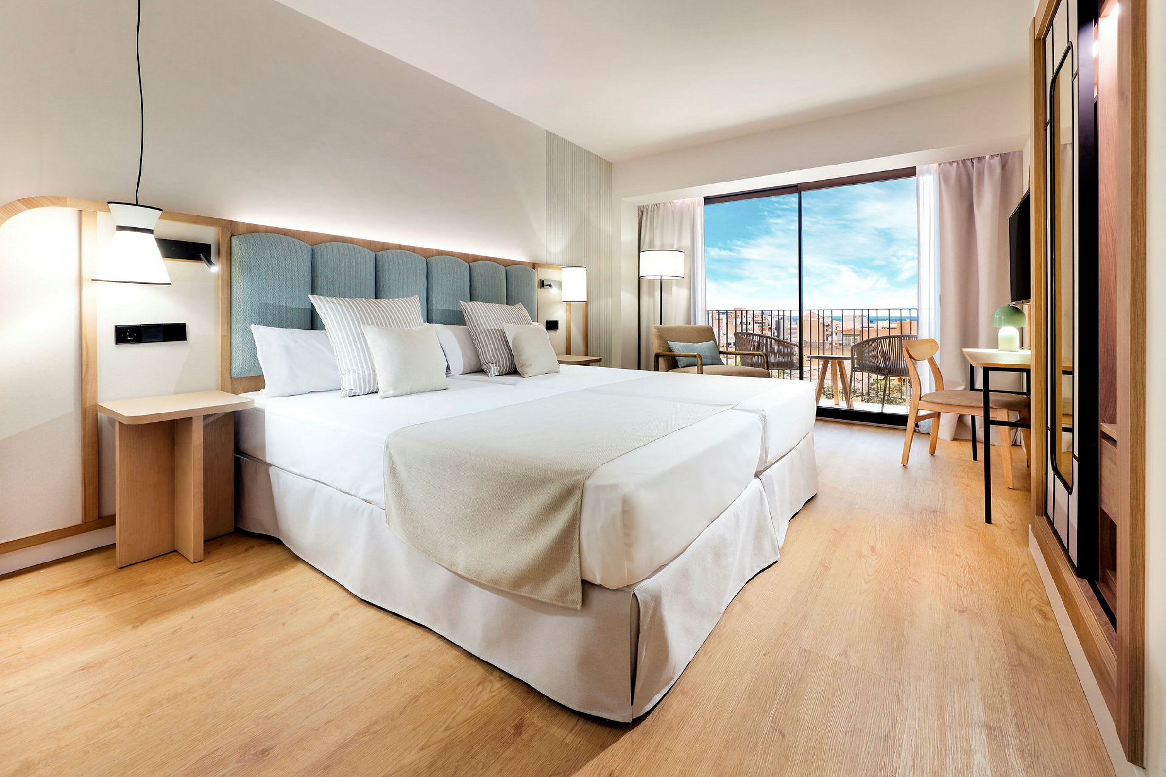 Hotellihuone, jossa on suuri pedattu sänky, vaaleasta puusta valmistettu paneeli ja suuri ikkuna näköalalla ulos. (Tekoälyn luoma teksti)
