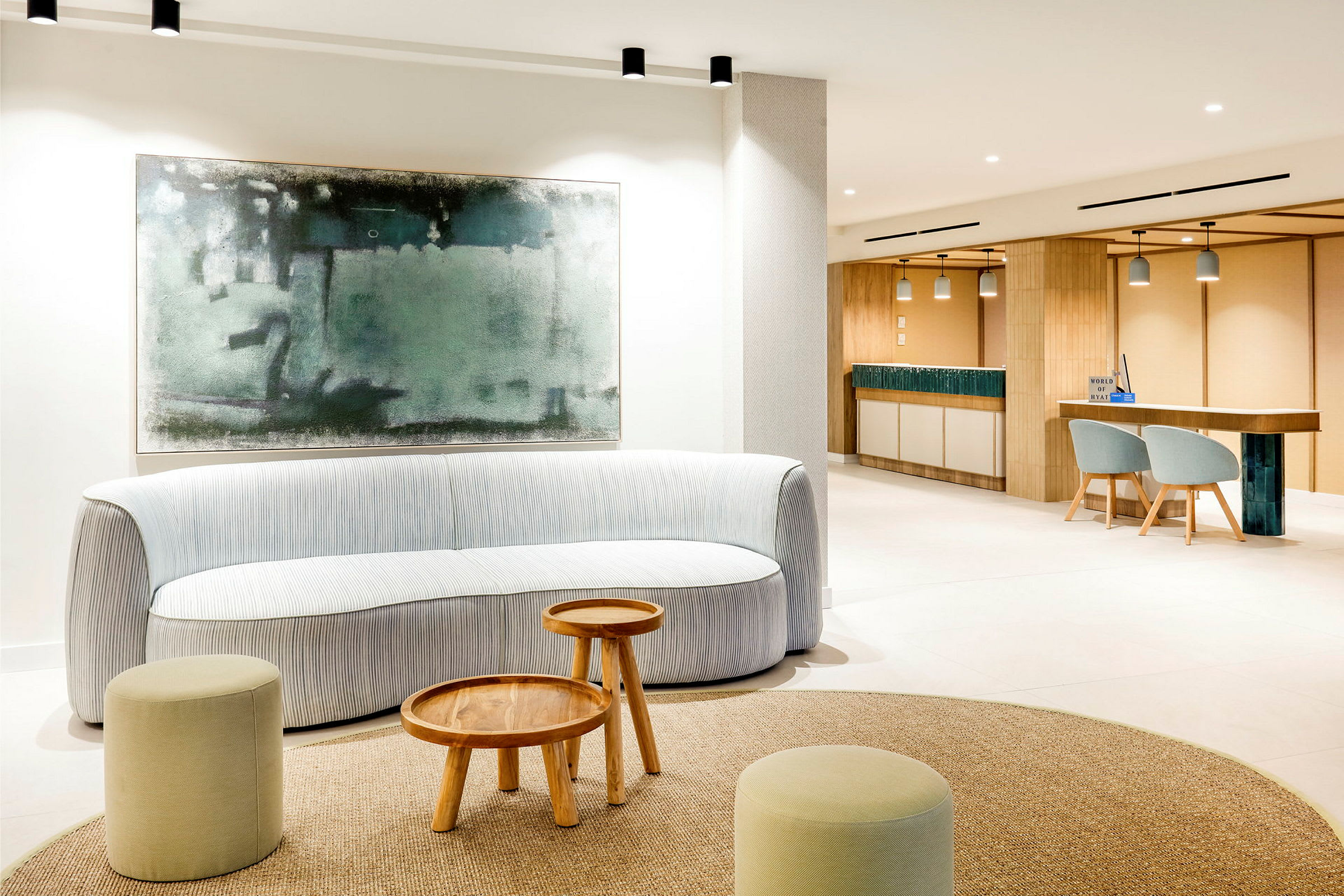 Valoisa, moderni lounge-tila, jossa sohva, pieniä puupöytiä ja raheja. Iso abstrakti taulu roikkuu seinällä sohvan takana. (Tekoälyn luoma teksti)