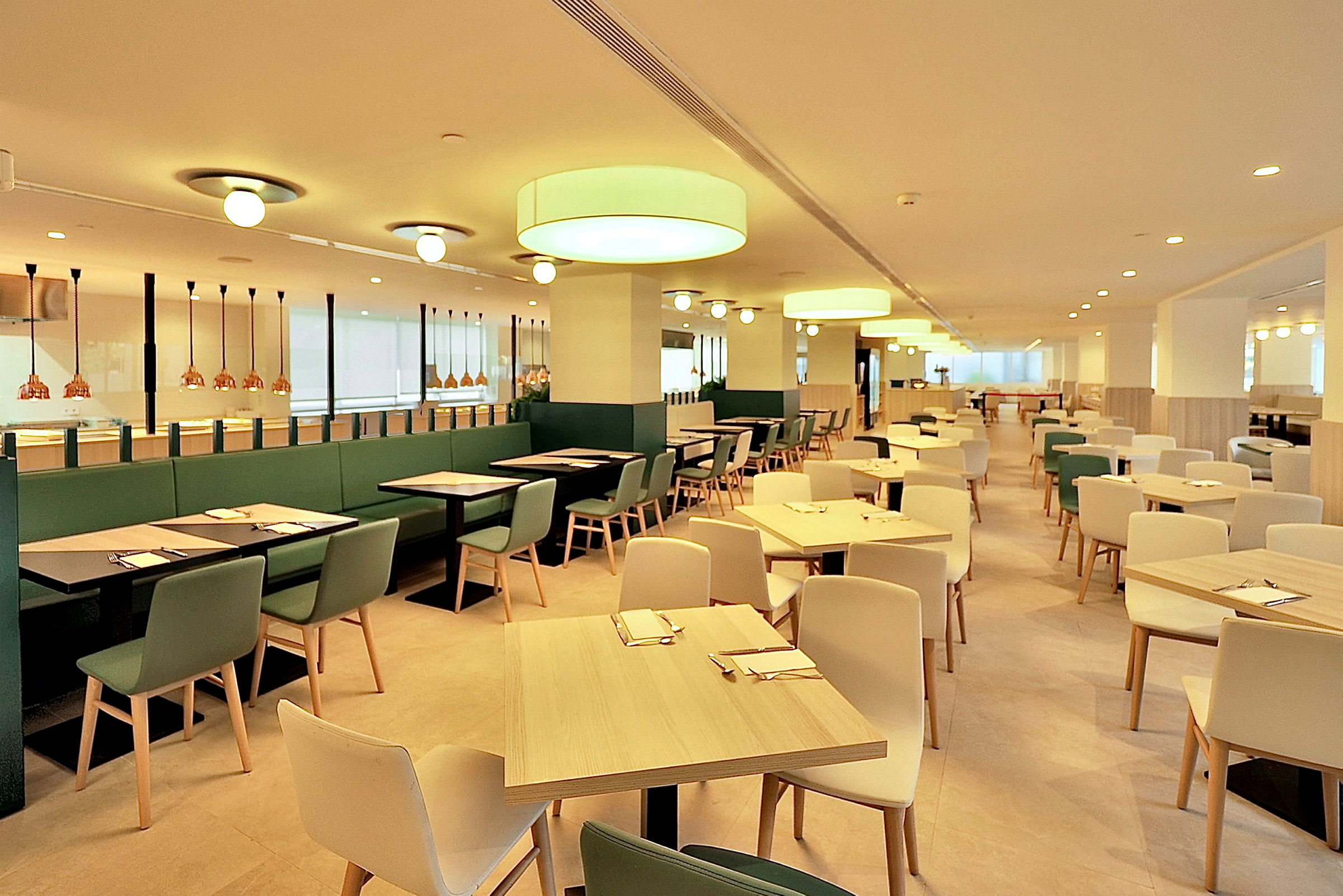 Valoisa ja tilava ravintola, jossa on modernit kalusteet ja valaistus. Pöydät ja tuolit on aseteltu tasaisiin riveihin. (Tekoälyn luoma teksti)
