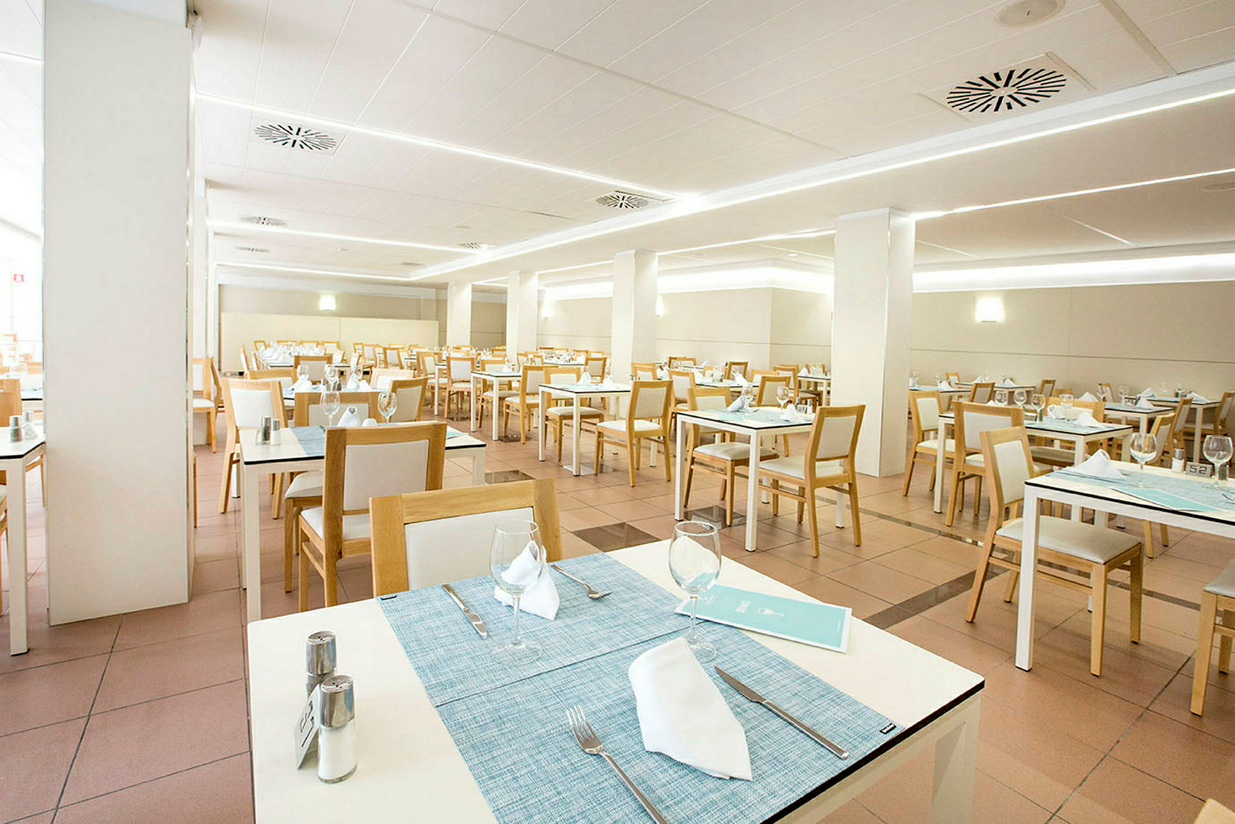Valoisa ja moderni ravintola, jossa on valkoisia pöytiä ja puutuoleja, valmiina asiakkaille. (Tekoälyn luoma teksti)