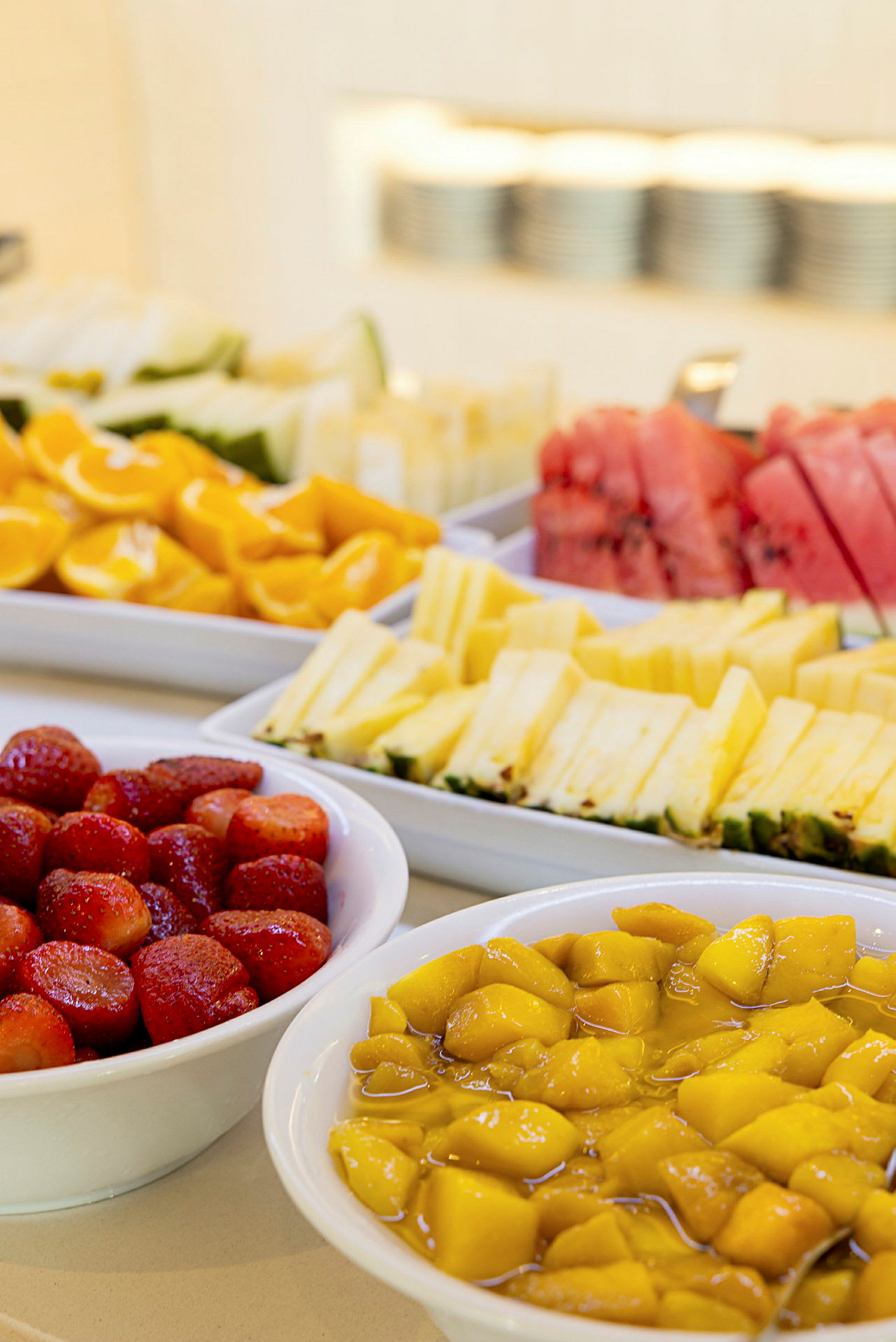 Pilkotut hedelmät, mukaan lukien mansikat, mango, melonit ja ananas, tarjoiltuna valkoisissa kulhoissa. (Tekoälyn luoma teksti)