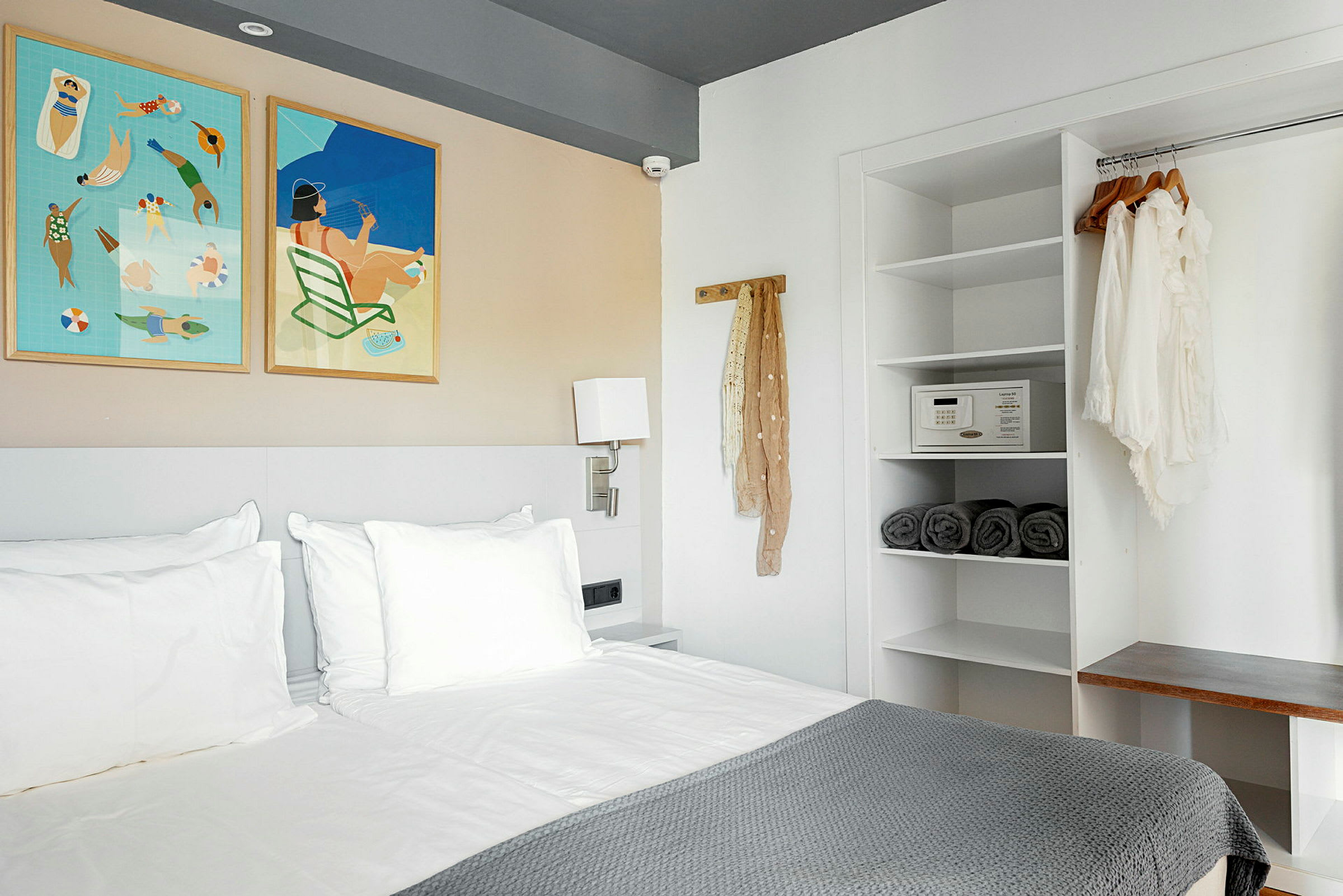 Moderni hotellihuone, jossa on sänky, seinään kiinnitettyjä tauluja ja avoin vaatekaappi. (Tekoälyn luoma teksti)