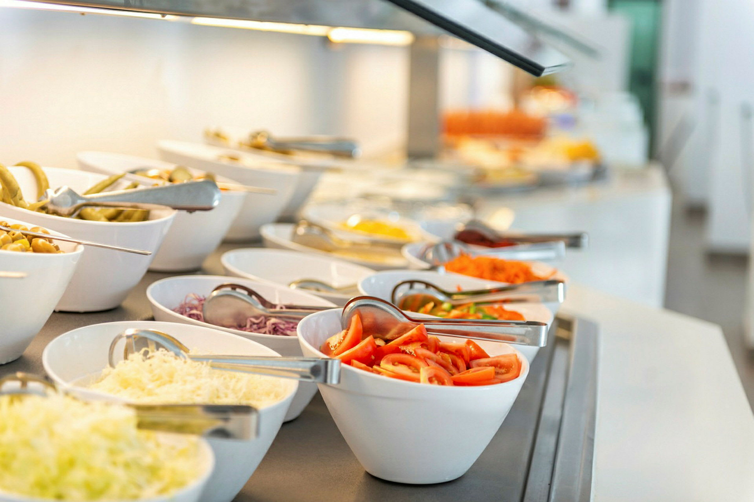Buffet, jossa eri salaattitarvikkeita valkoisissa kulhoissa. (Tekoälyn luoma teksti)