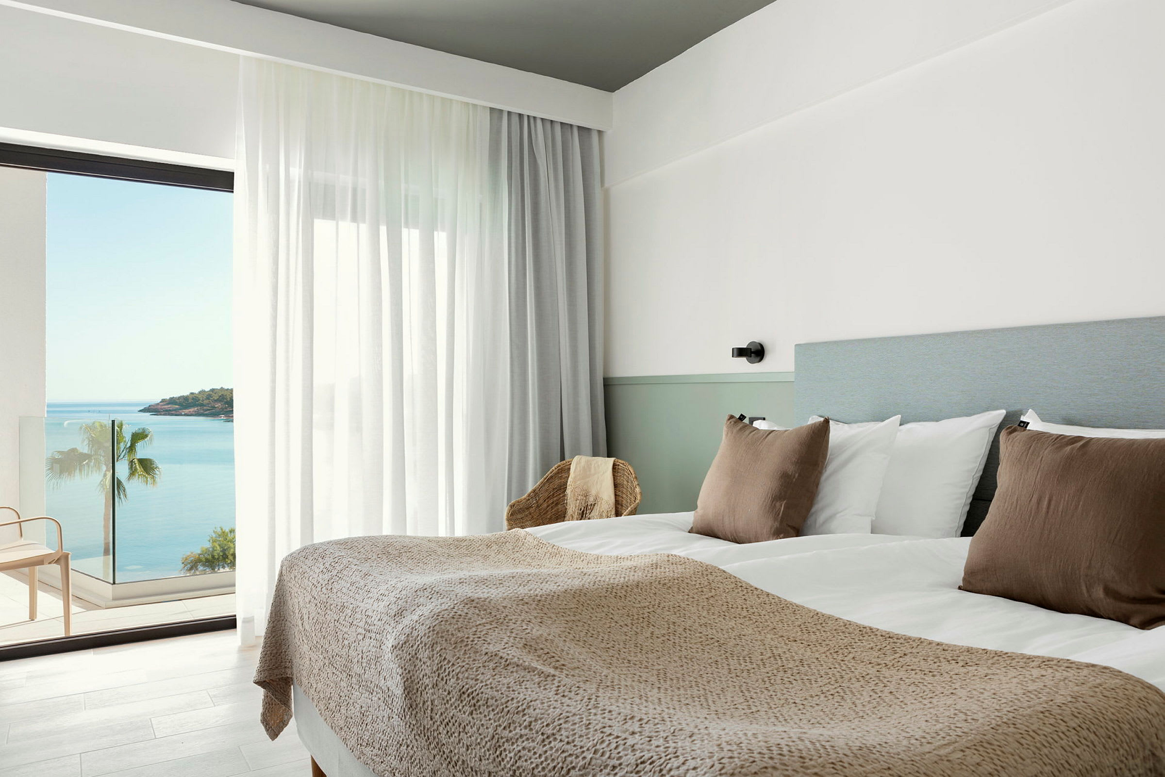 Hotellihuone, jossa on parivuode, vaaleat värit ja merinäkymä parvekkeelta. (Tekoälyn luoma teksti)