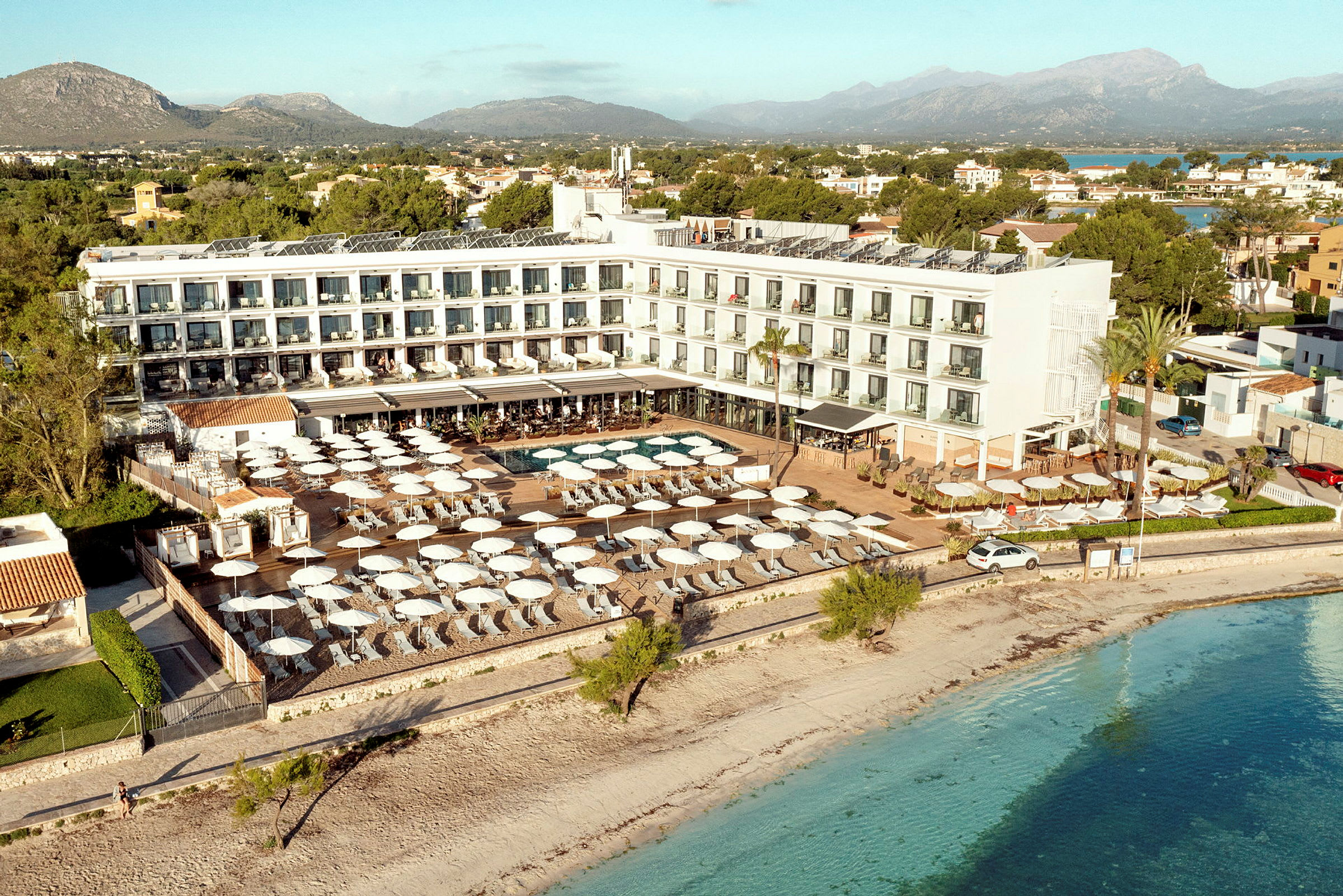 Ilmakuva hotellista rannalla, jossa on uima-allasalue ja aurinkovarjoja. (Tekoälyn luoma teksti)