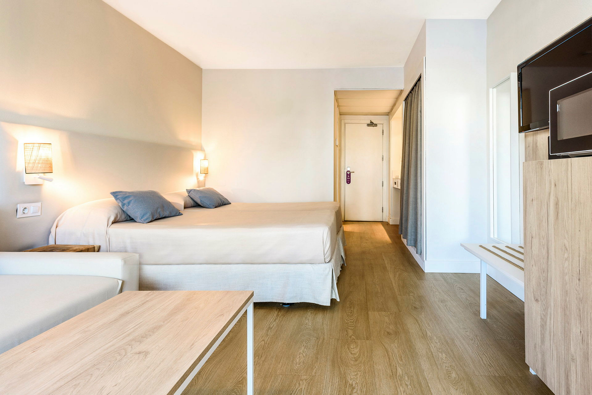 Hotellihuone, jossa on parivuode, sohva, puinen pöytä, televisio ja ovi kylpyhuoneeseen. (Tekoälyn luoma teksti)