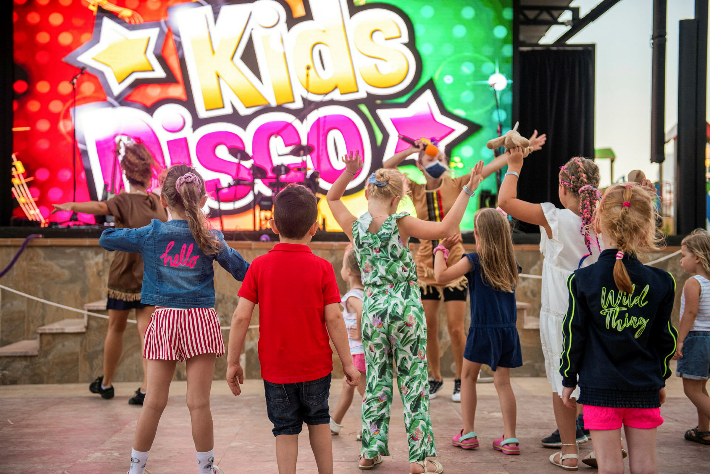 Lapsia tanssimassa värikkään kyltin edessä, jossa lukee 'Kids Disco'. (Tekoälyn luoma teksti)