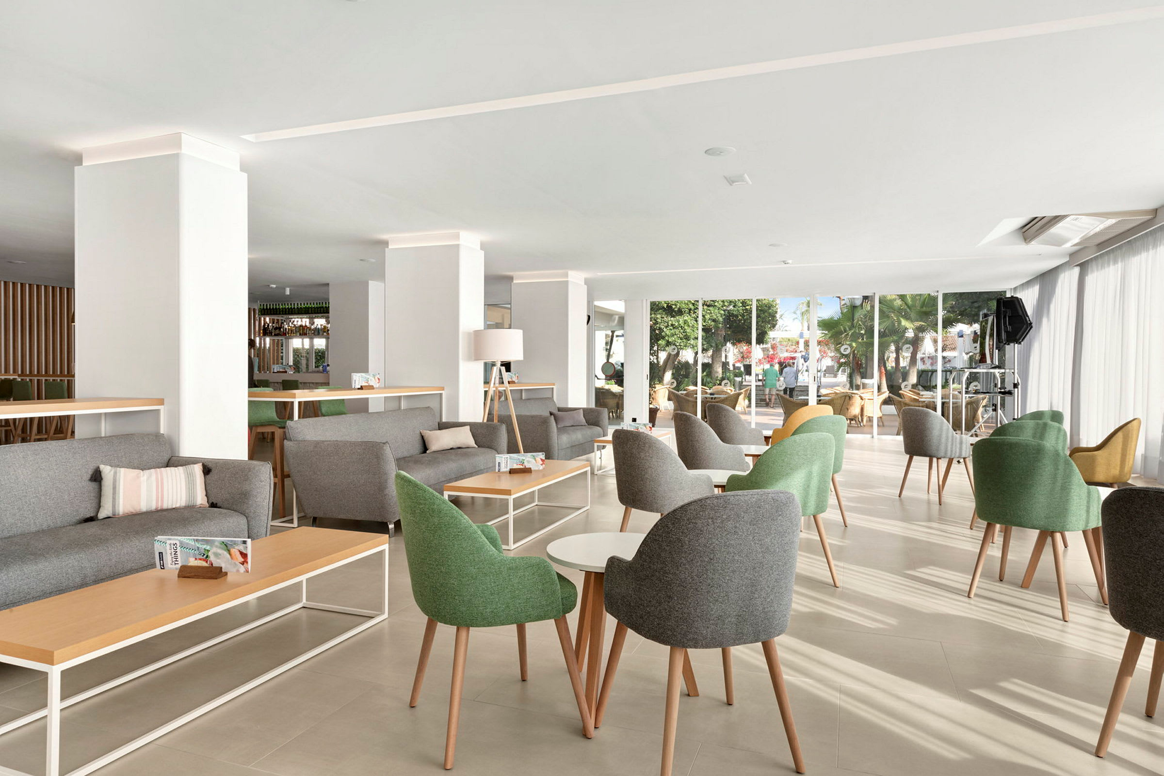 Valoisa ja moderni lounge, jossa on vihreitä ja harmaita tuoleja, pöytiä ja suuria ikkunoita. (Tekoälyn luoma teksti)