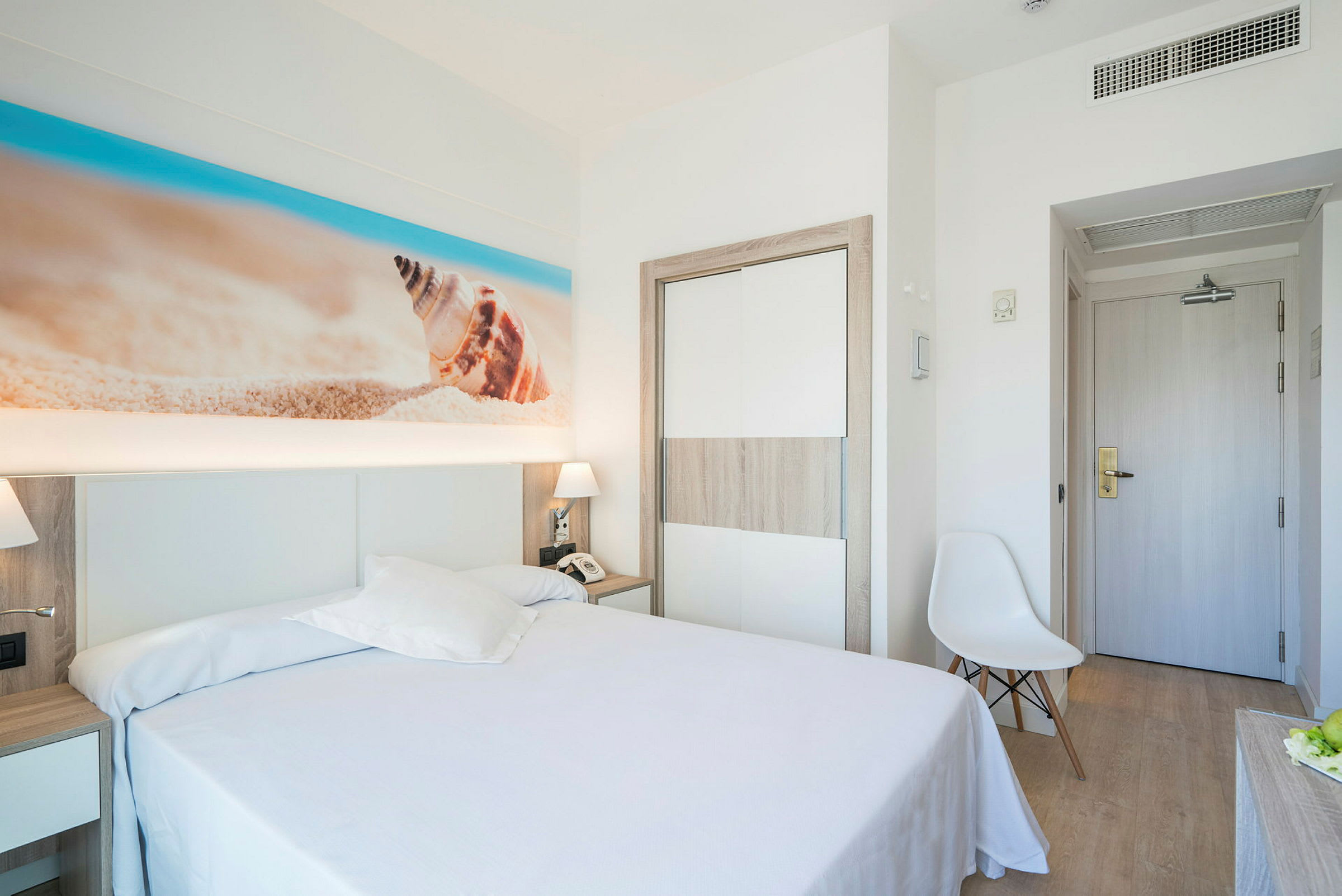 Hotellihuone, jossa on parivuode ja seinällä hiekkaranta-aiheinen taideteos. (Tekoälyn luoma teksti)