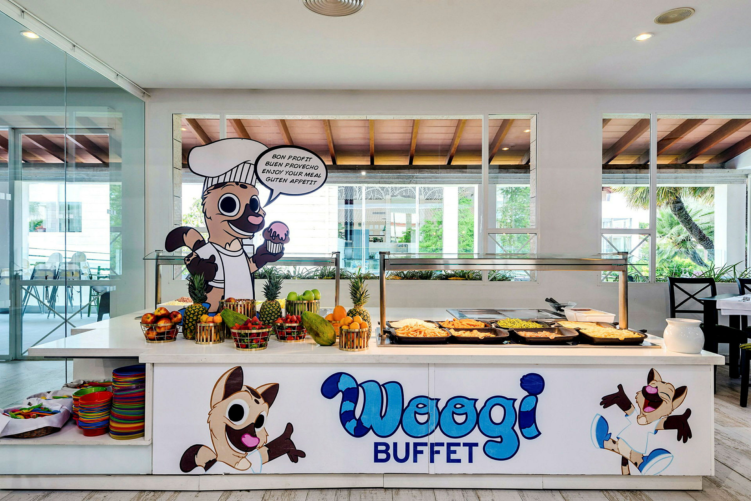Buffetpöytä erilaisilla ruoilla, tuoreilla hedelmillä ja sarjakuvahahmoilla tekstillä 'Woogi Buffet'. (Tekoälyn luoma teksti)