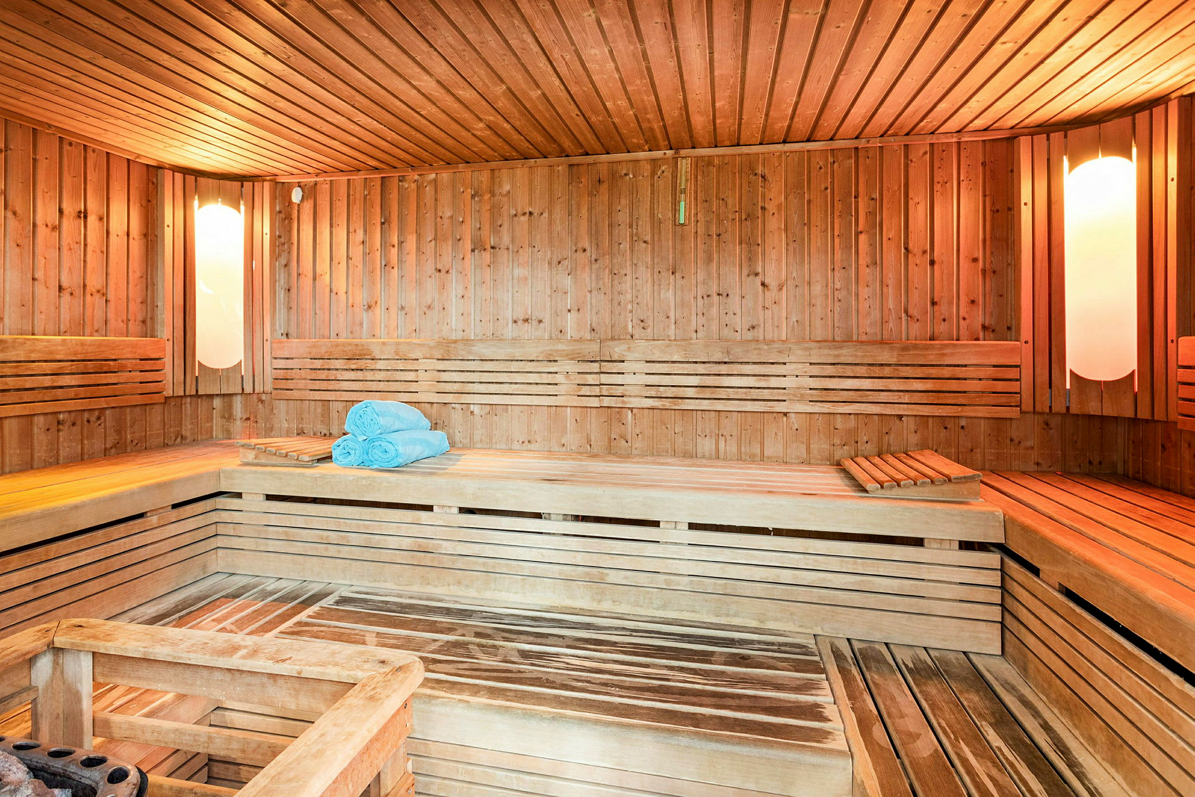 Sauna, jossa on puupaneelit, istuinpenkit ja sinisiä pyyhkeitä asetettuna yhdelle penkille. (Tekoälyn luoma teksti)