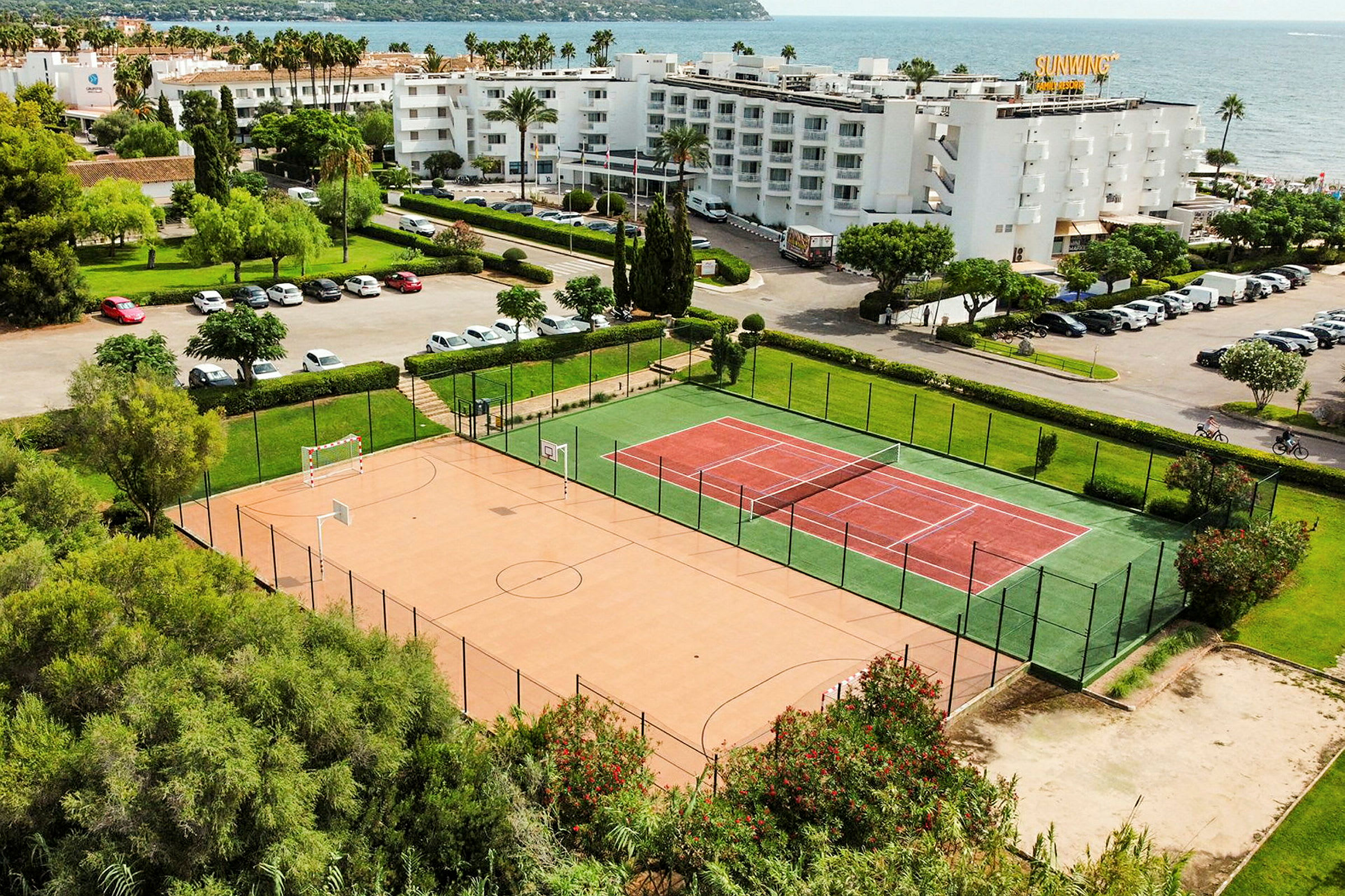Kuva tennis- ja urheilualueesta meren läheisyydessä, taustalla rakennuksia ja pysäköintipaikkoja. (Tekoälyn luoma teksti)