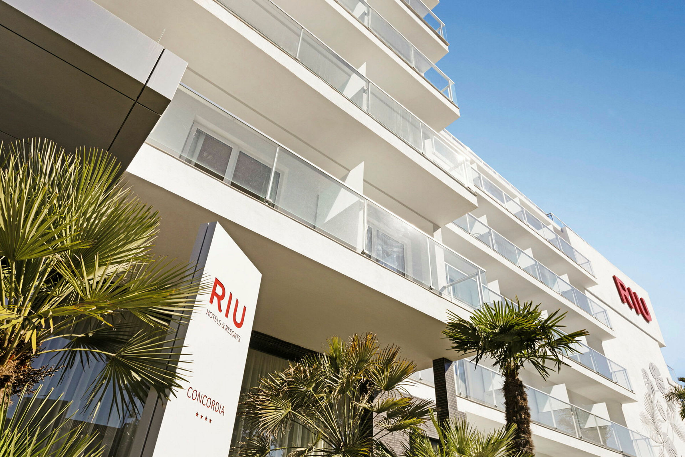 Moderni hotellirakennus parvekkeineen ja palmuja etualalla. (Tekoälyn luoma teksti)