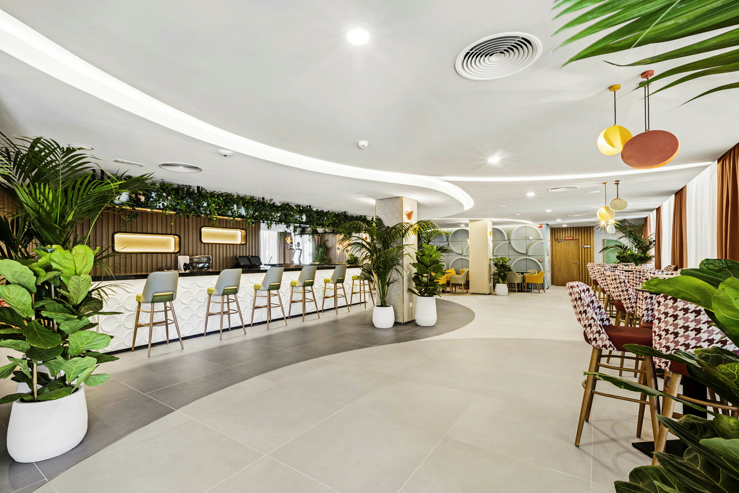 Moderni lounge, jossa on baari ja useita istumapaikkoja. Kasveja käytetään sisustuksena. (Tekoälyn luoma teksti)