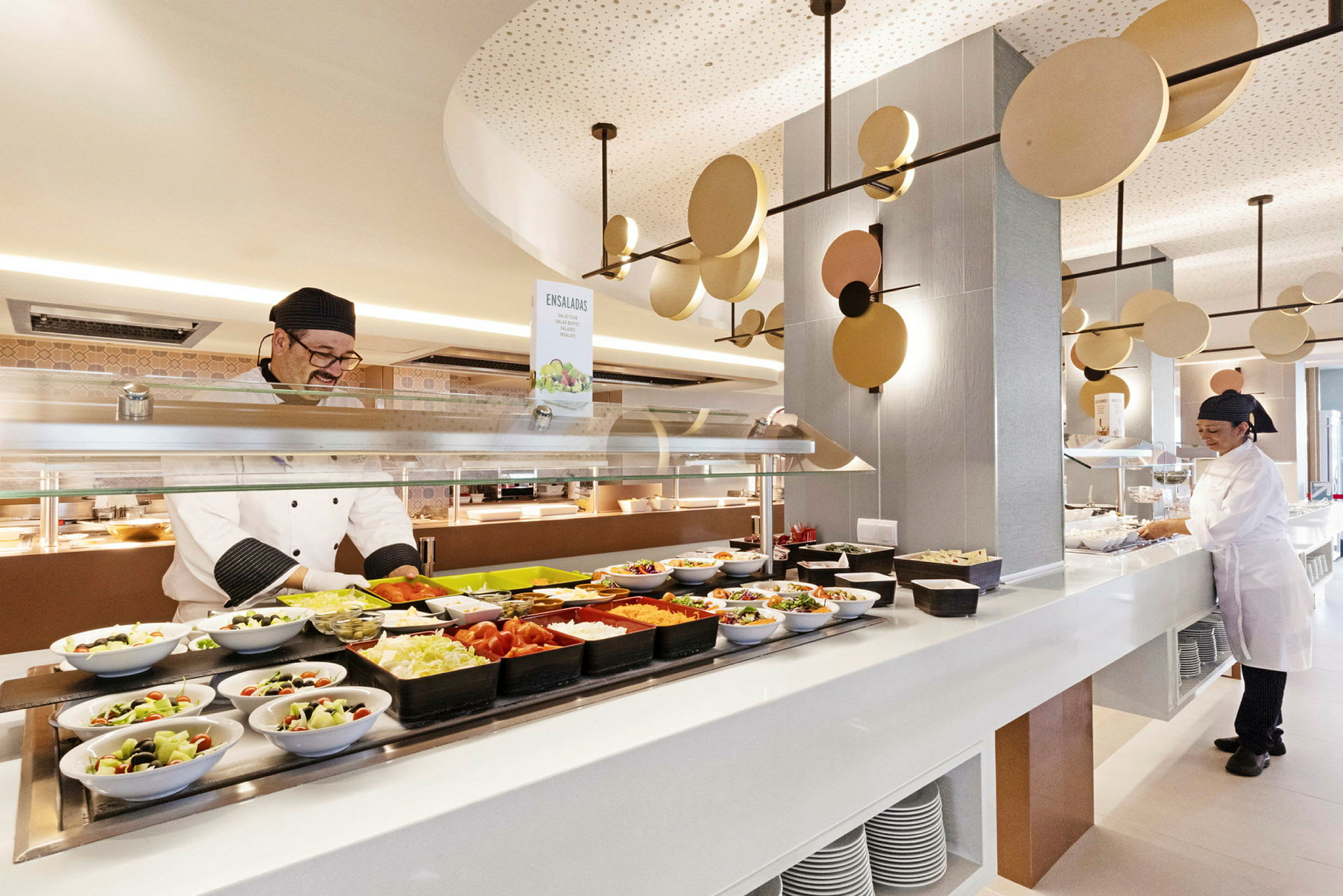 Buffet, jossa on salaatteja ja lisukkeita, tarjoillaan valoisassa ja modernissa ravintolassa. (Tekoälyn luoma teksti)