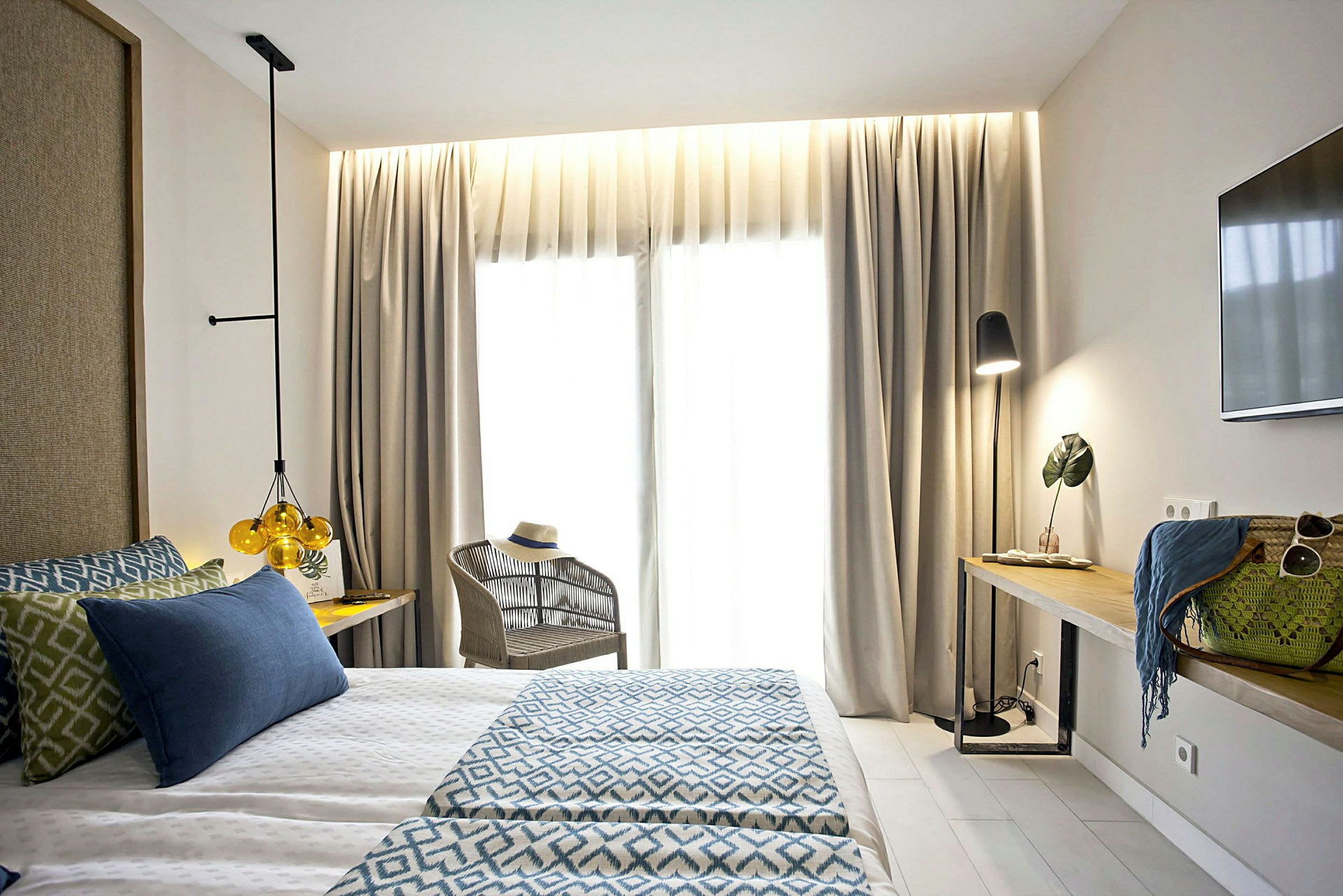 Valoisa hotellihuone, jossa on parivuode, nojatuoli ja pöytä koriste-esineineen ja lampulla. (Tekoälyn luoma teksti)