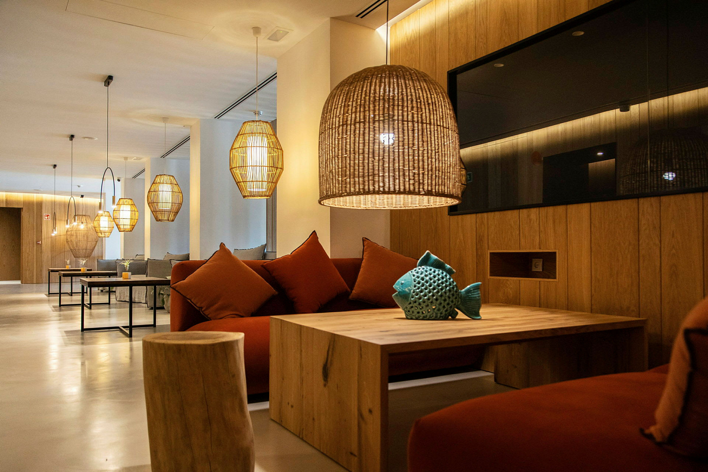 Moderni lounge, jossa sohvia, puisia pöytiä ja roikkuvia lamppuja. (Tekoälyn luoma teksti)