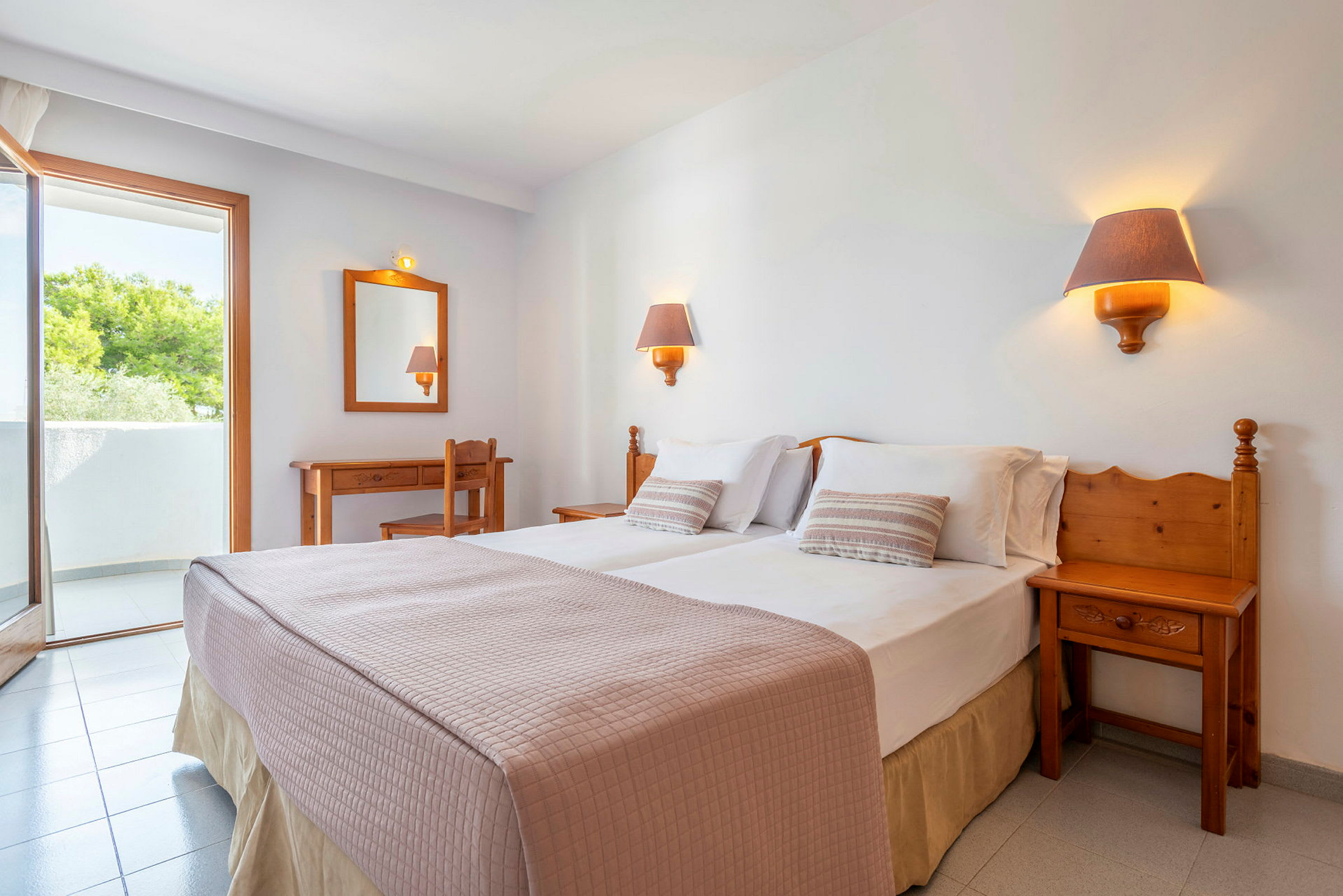Hotellihuone, jossa on parivuode, kaksi yöpöytälamppua, työpöytä, tuoli ja parveke. (Tekoälyn luoma teksti)