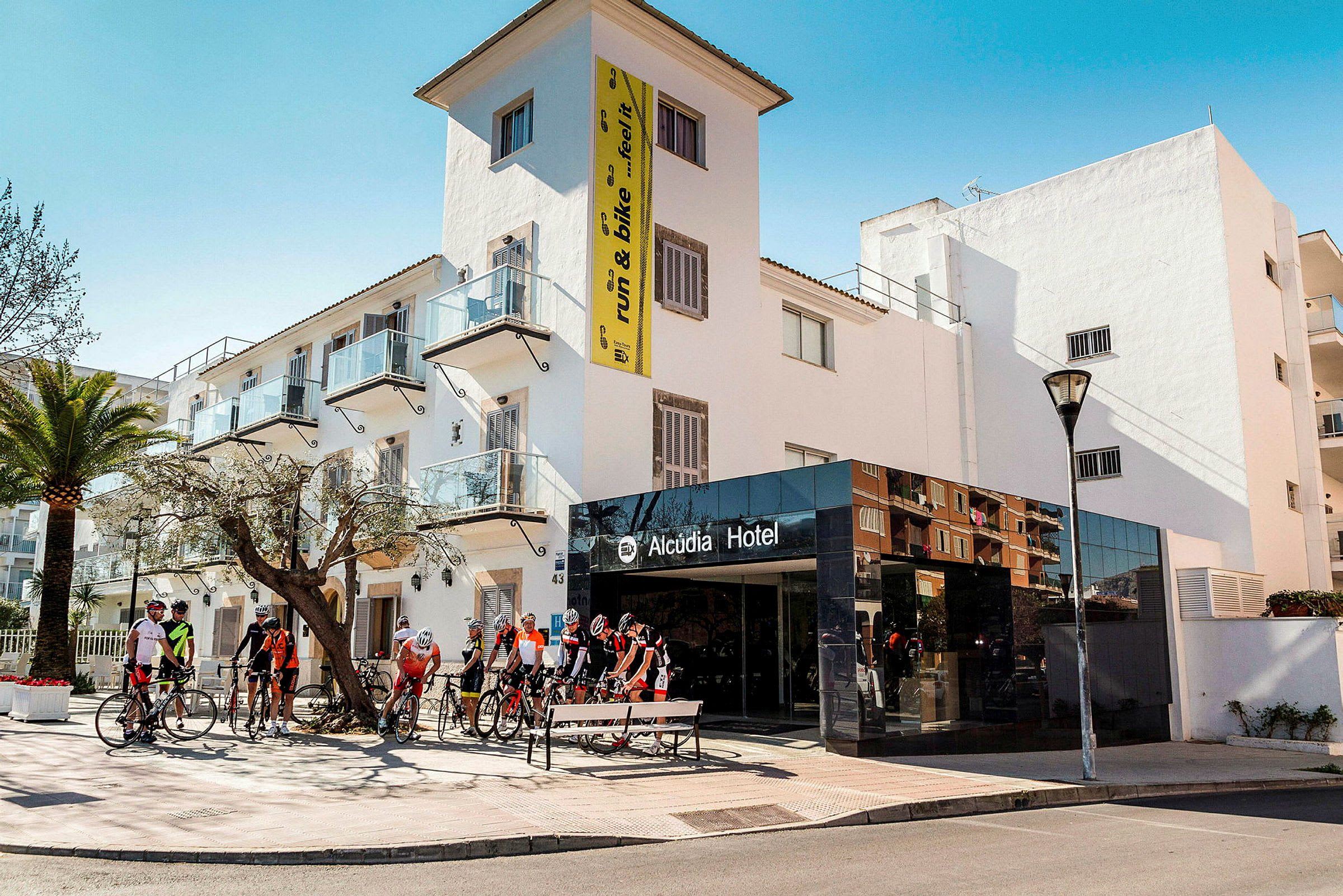 Näkymä Alcudia-hotellista, pyöräilijöitä kokoontuneena sisäänkäynnin eteen. (Tekoälyn luoma teksti)