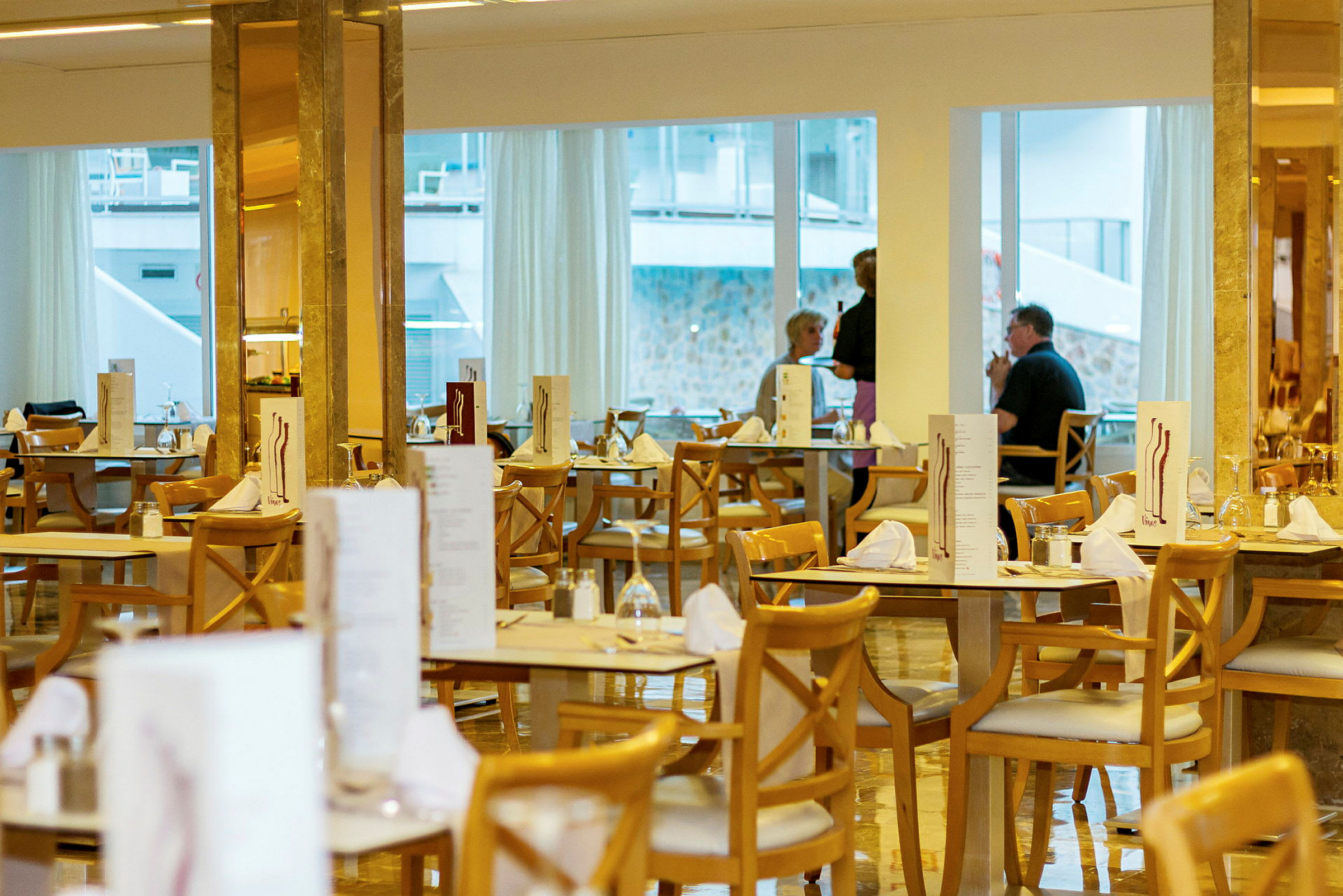 Ravintola, jossa katetut pöydät ja puutuolit, taustalla ikkunat. (Tekoälyn luoma teksti)