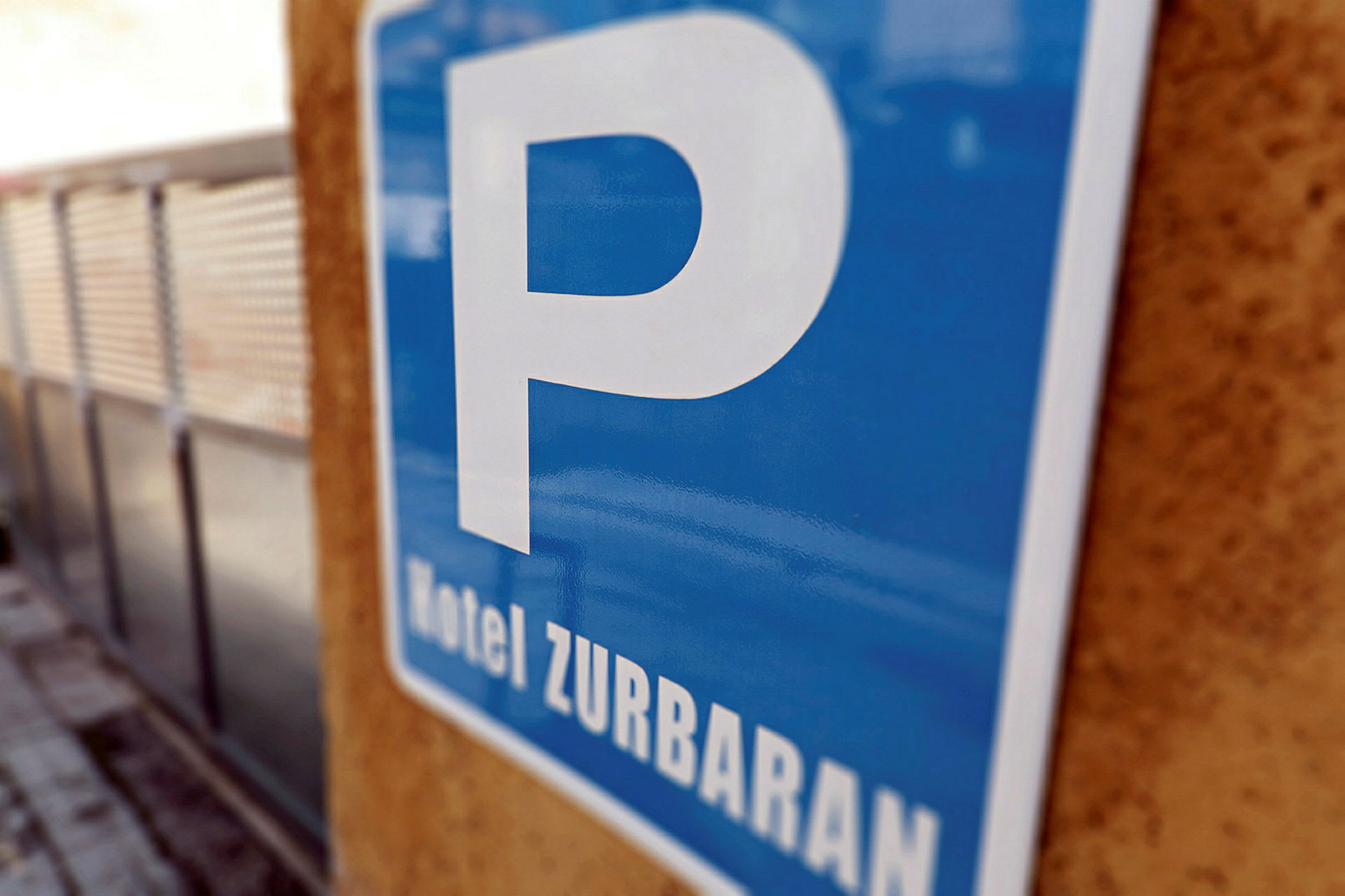 Sininen pysäköintikyltti, jossa lukee 'Hotel Zurbaran', kiinnitettynä seinään. (Tekoälyn luoma teksti)