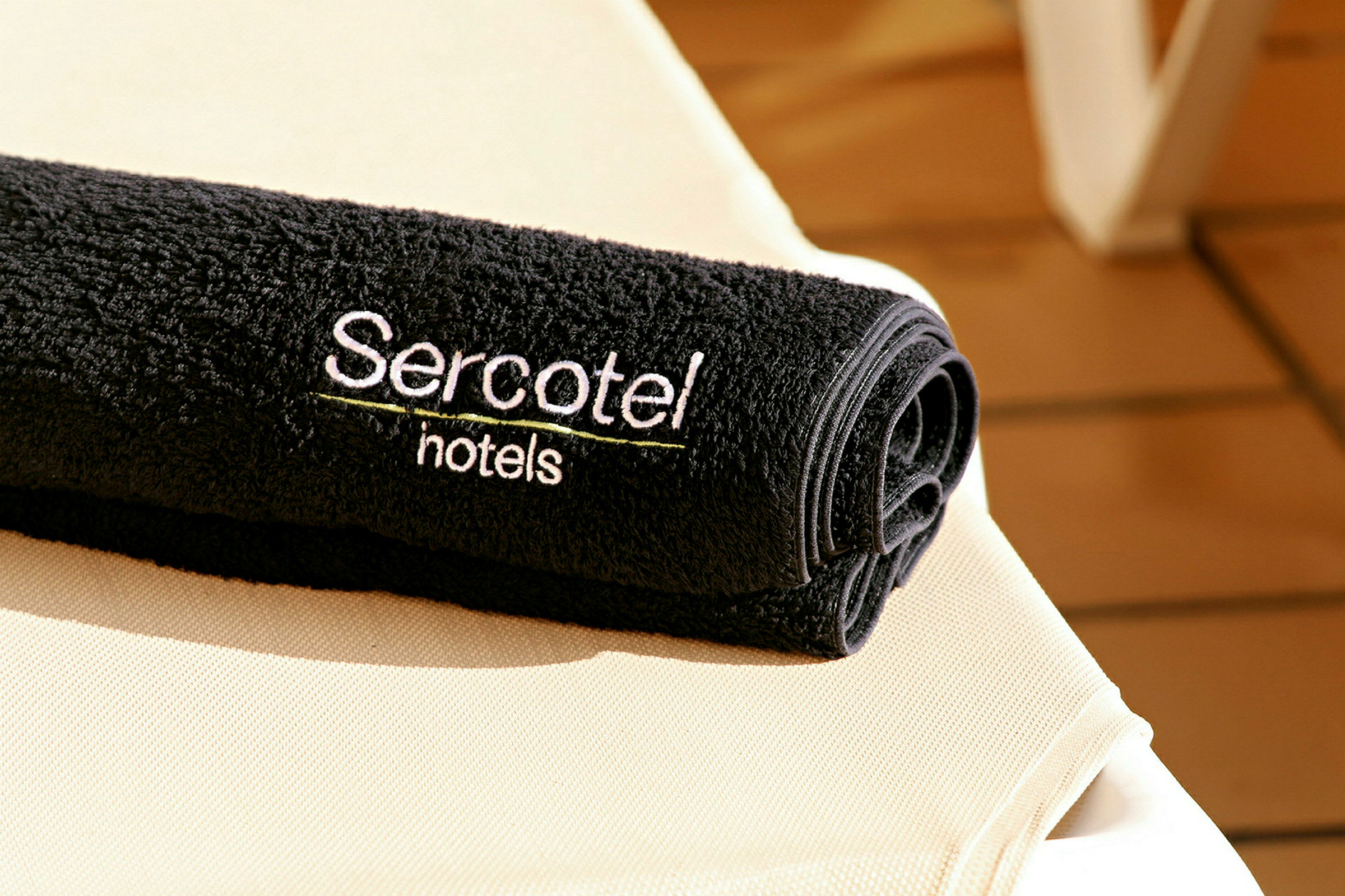 Musta pyyhe, jossa on brodeerattu teksti 'Sercotel hotels', asetettuna vaalealle pinnalle. (Tekoälyn luoma teksti)