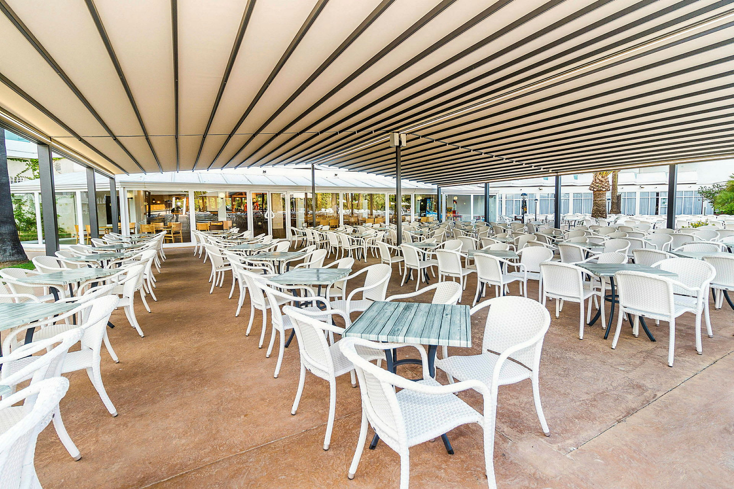 Ulkona oleva ravintola, jossa on paljon valkoisia pöytiä ja tuoleja katon alla. (Tekoälyn luoma teksti)