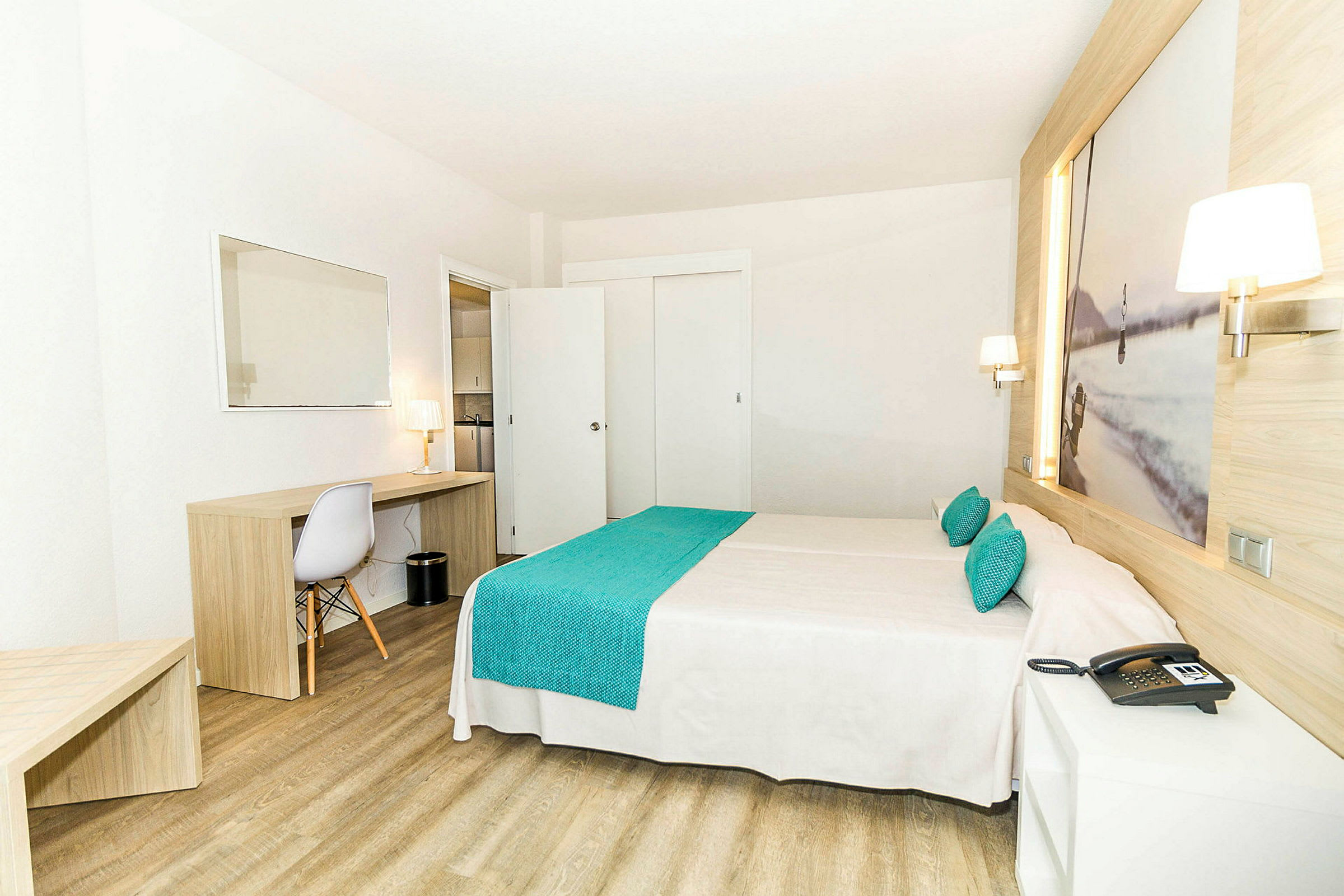Hotellihuone, jossa on parisänky, puukalusteet ja työpöytä tuoleineen ja lampulla varustettuna. (Tekoälyn luoma teksti)