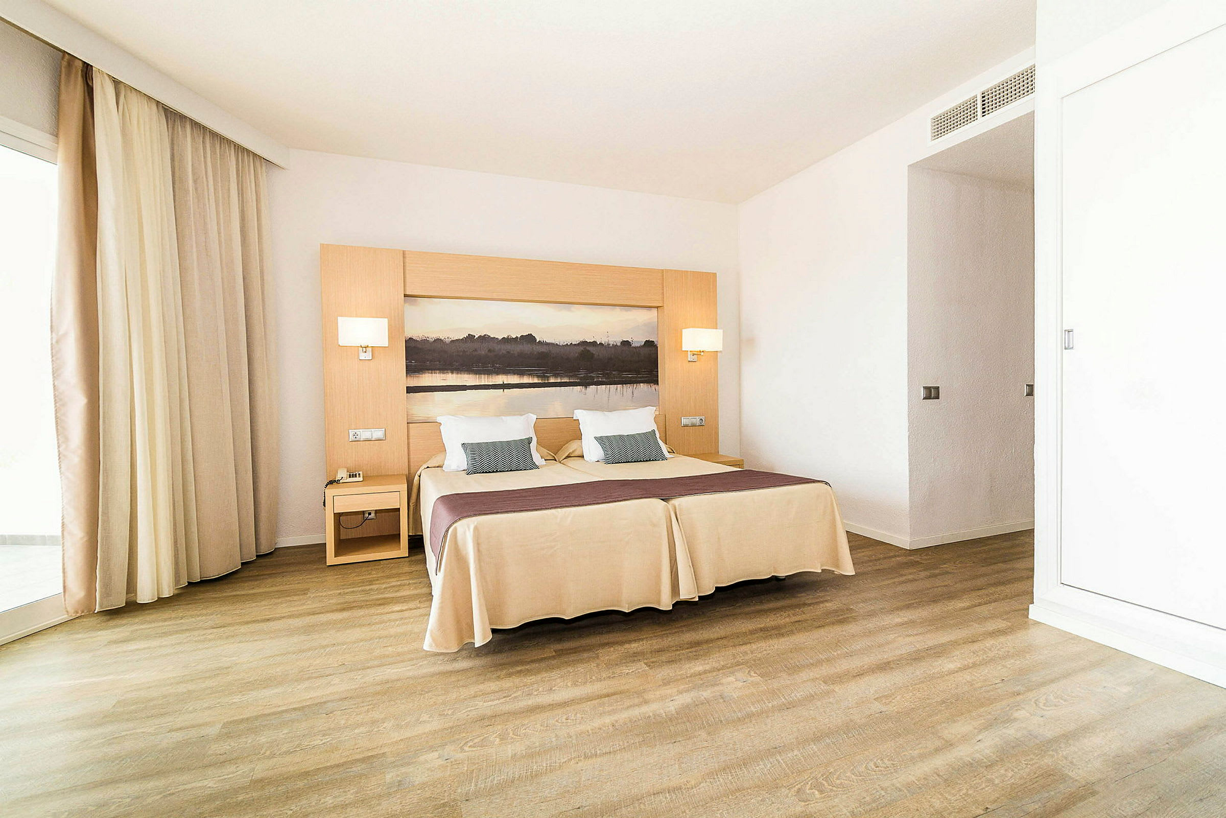 Hotellihuone, jossa parivuode, kaksi yöpöytää ja luonnonmaalaus sängyn takana. (Tekoälyn luoma teksti)