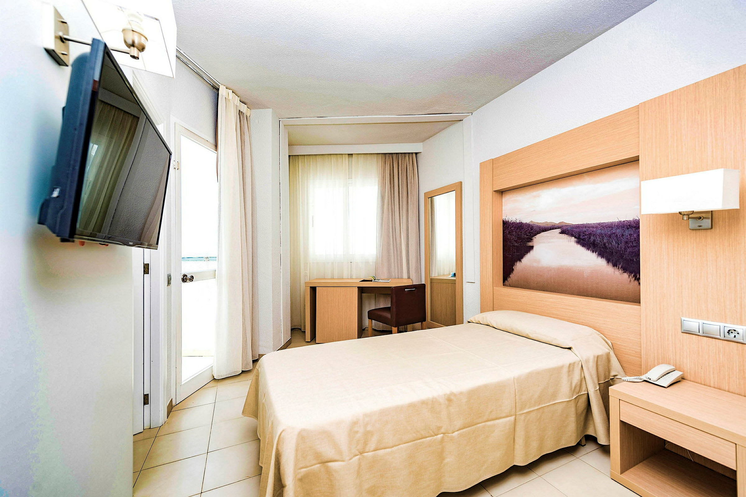 Hotellihuone, jossa on yhden hengen sänky, työpöytä ja seinälle kiinnitetty TV. (Tekoälyn luoma teksti)