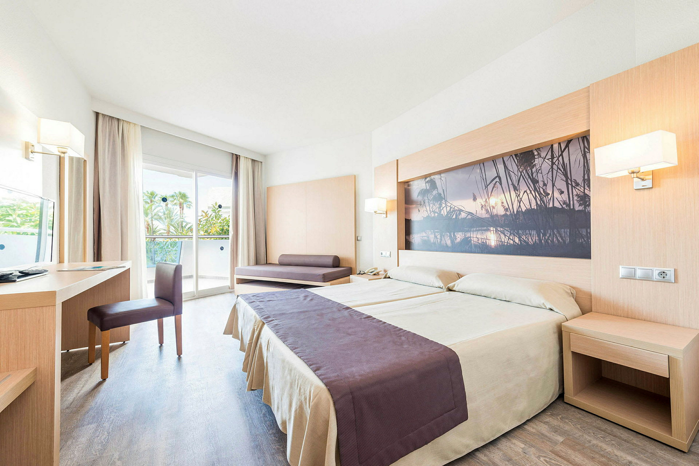Hotellihuone, jossa on parivuode, kirjoituspöytä, tuoli ja sohva. Huoneessa on lasiovi, joka johtaa parvekkeelle. (Tekoälyn luoma teksti)