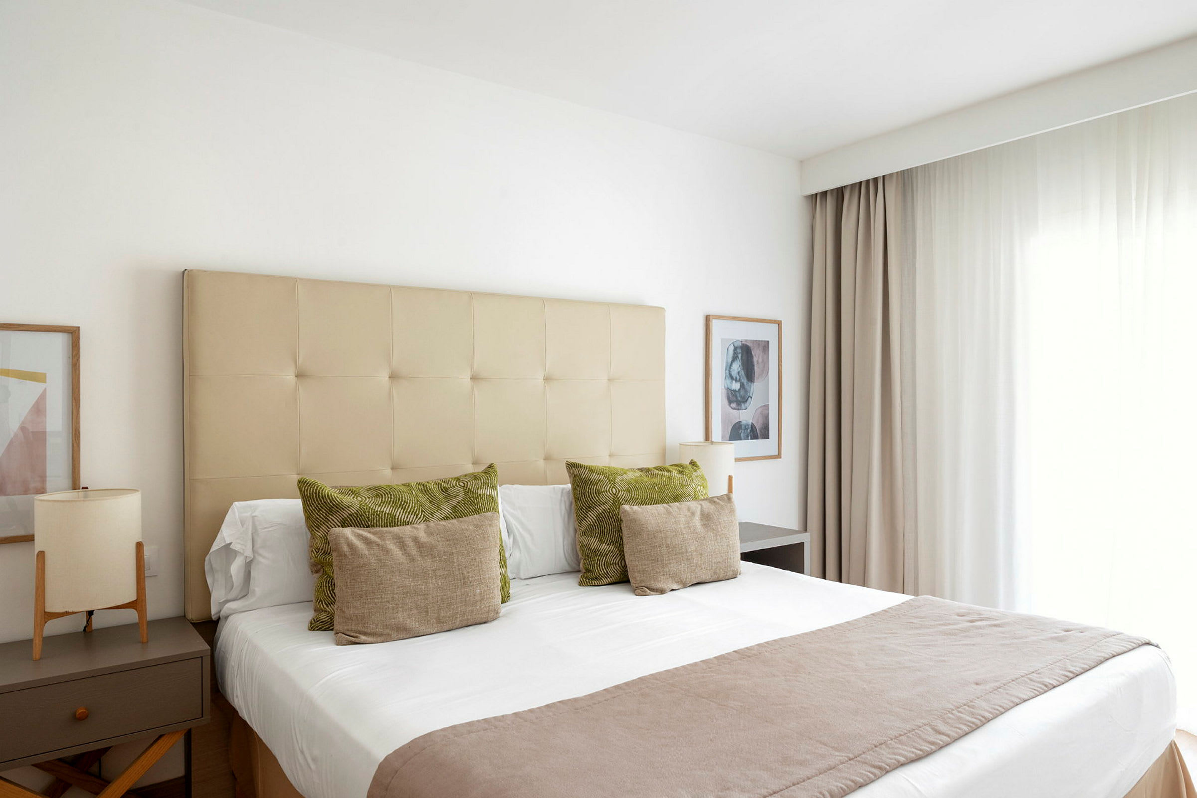 Valoisa ja tyylikäs hotellihuone, jossa on pedattu sänky. Verho oikealla ja yöpöytä vasemmalla. (Tekoälyn luoma teksti)