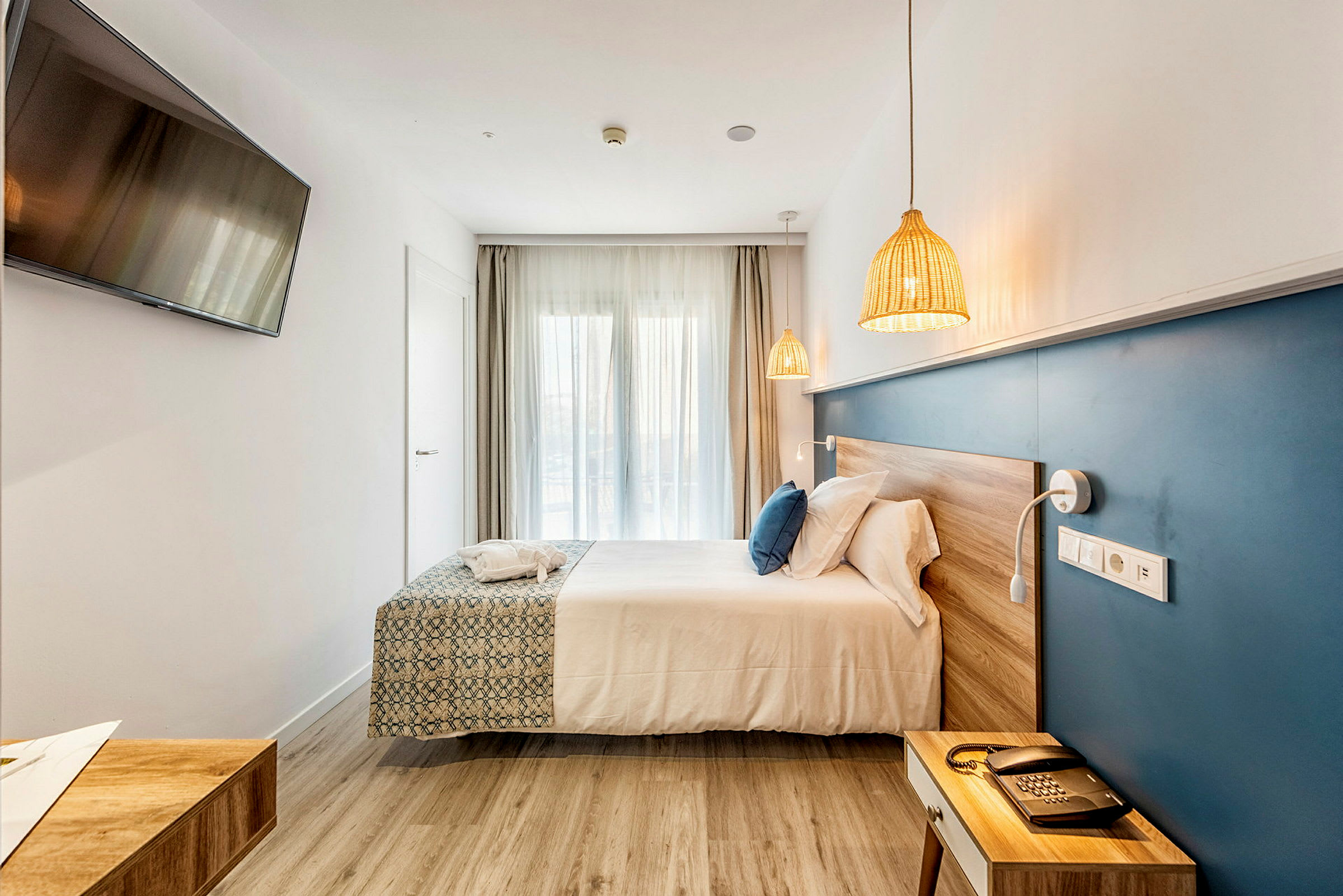 Hotellihuone, jossa on parivuode, sininen seinäpaneeli, televisio seinällä ja luonnolliset puupinnat. (Tekoälyn luoma teksti)