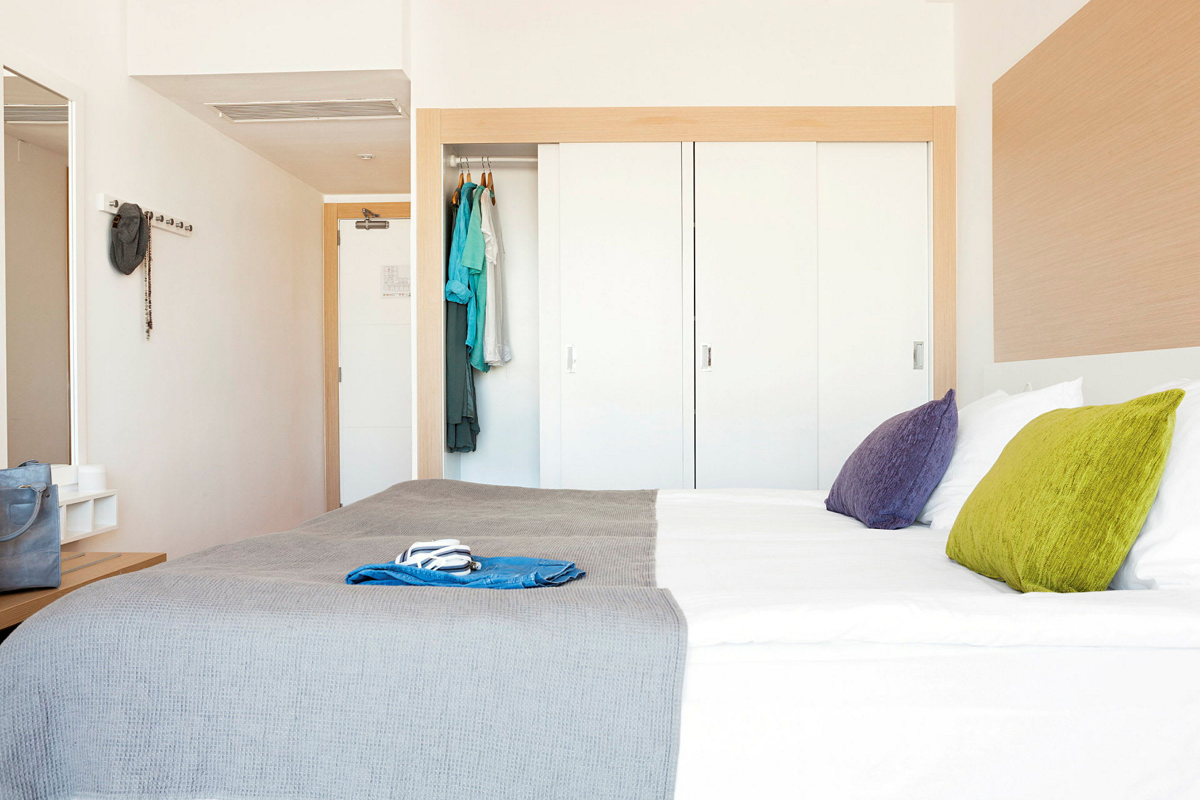 Hotellihuone, jossa on parivuode, värikkäät tyynyt ja vaatekaappi. (Tekoälyn luoma teksti)